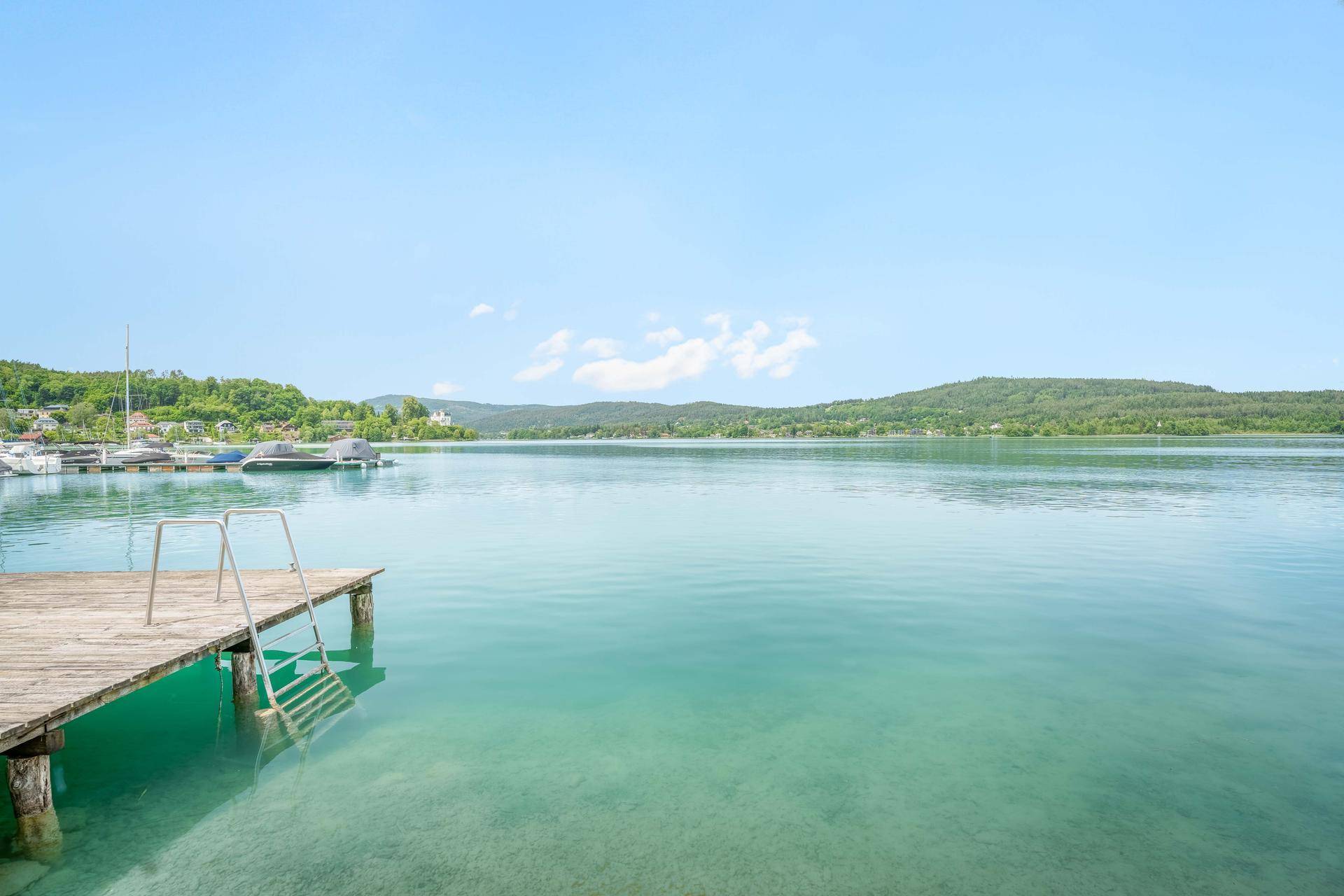 Malerischer Blick auf den See mit einem Holzsteg und Booten unter blauem Himmel.