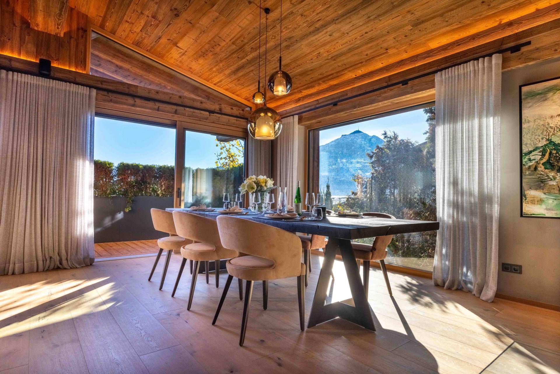 Heller Essbereich mit Holztisch, großen Fenstern und Panoramablick auf die umliegende Berglandschaft.