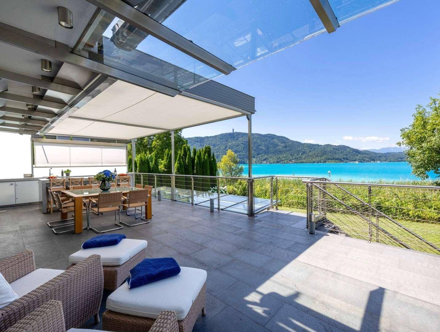 Geräumige Terrasse mit Lounge-Möbeln, Sonnenschutz und beeindruckendem Blick auf den See und die Berge.