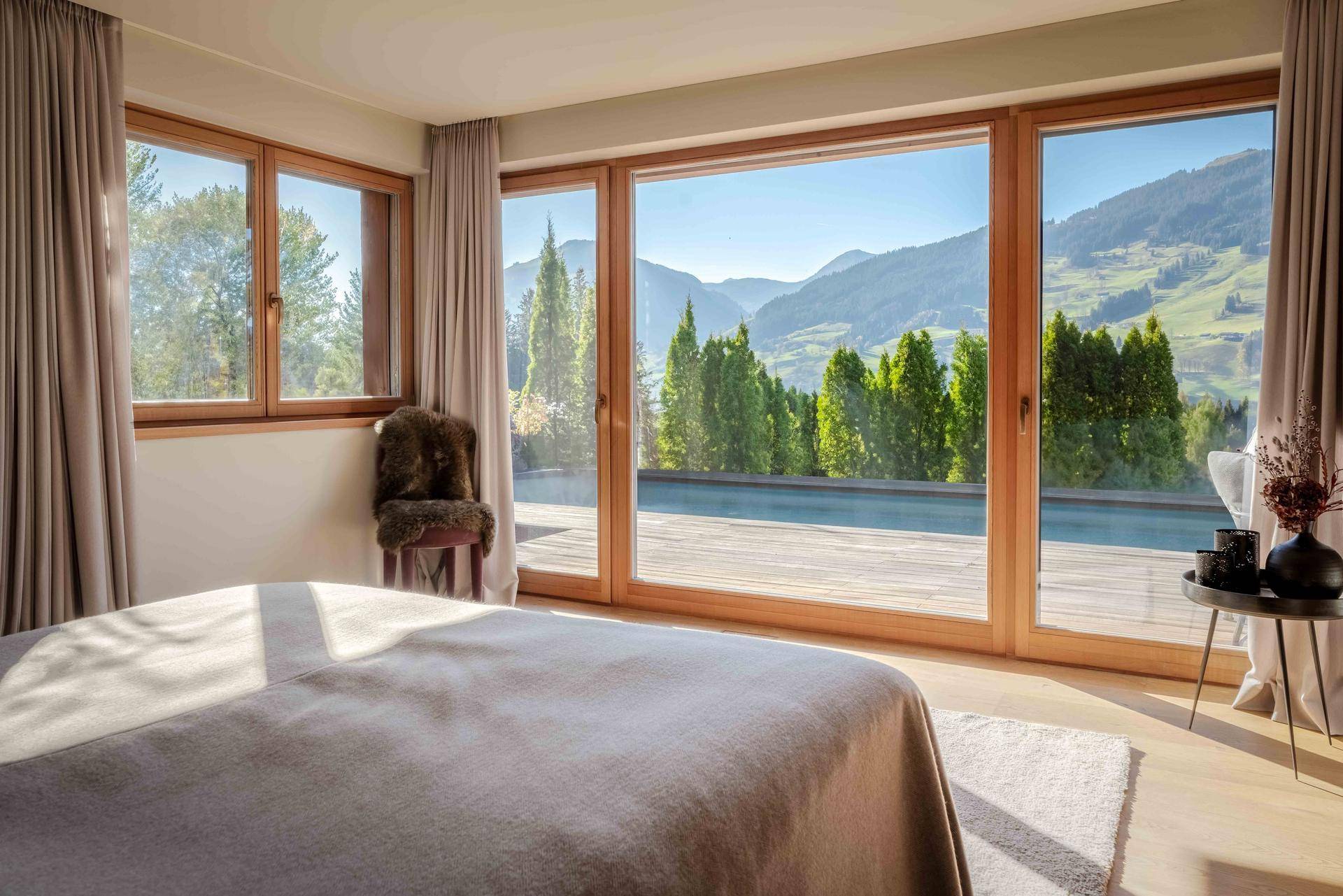 Helles Schlafzimmer mit großen Fenstern und direktem Blick auf den Pool und die Berge.