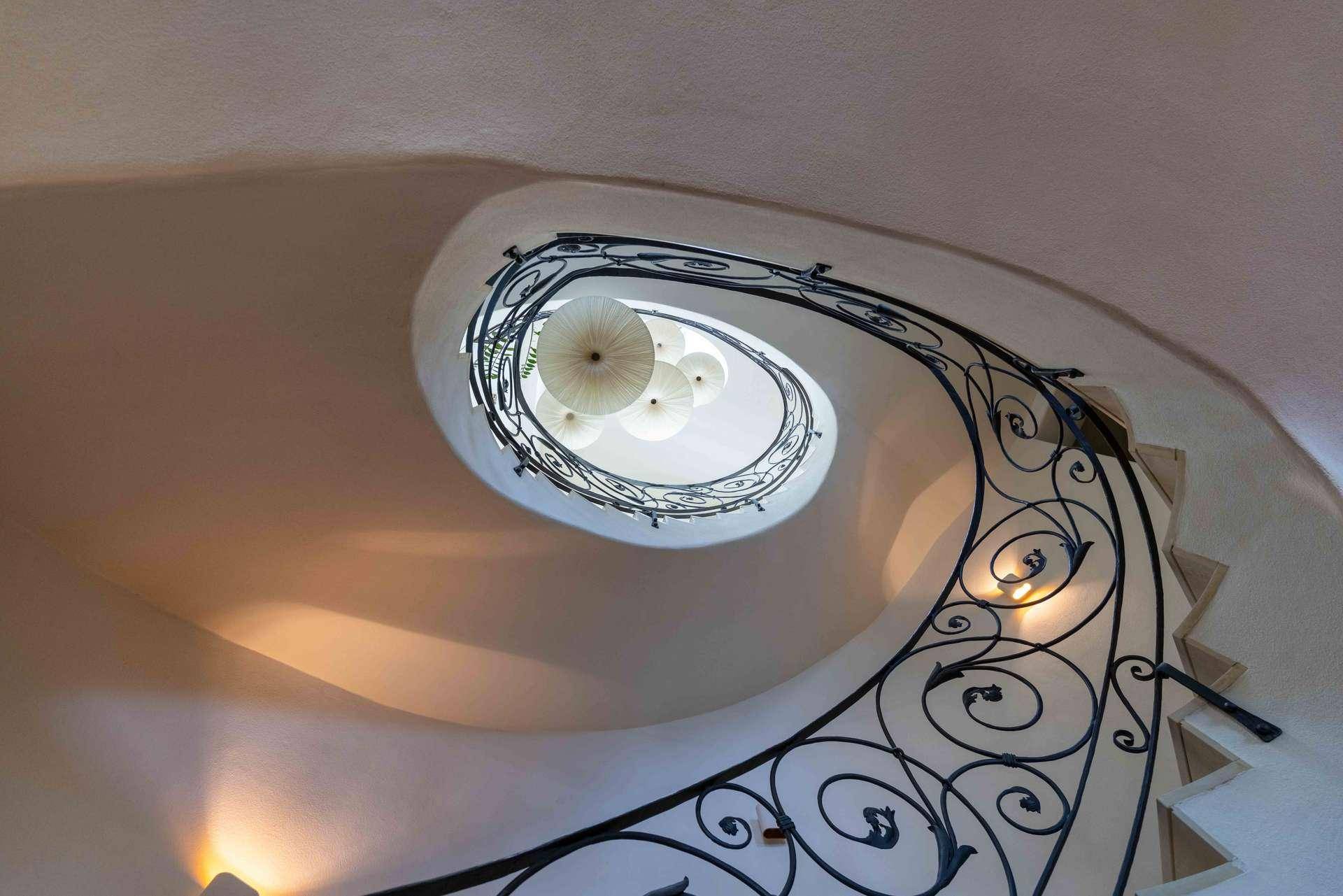 Elegante Wendeltreppe mit kunstvollem schmiedeeisernem Geländer und stilvoller Deckenbeleuchtung.