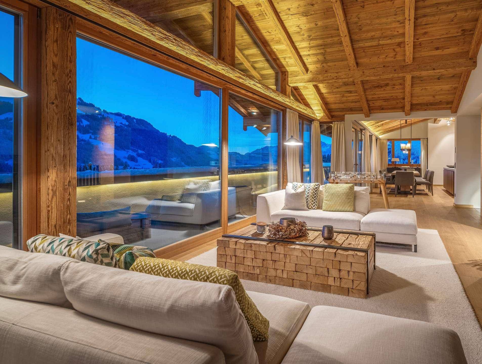 Geräumiges Wohnzimmer mit großen Panoramafenstern, Holzbalkendecke und gemütlicher Sitzecke.