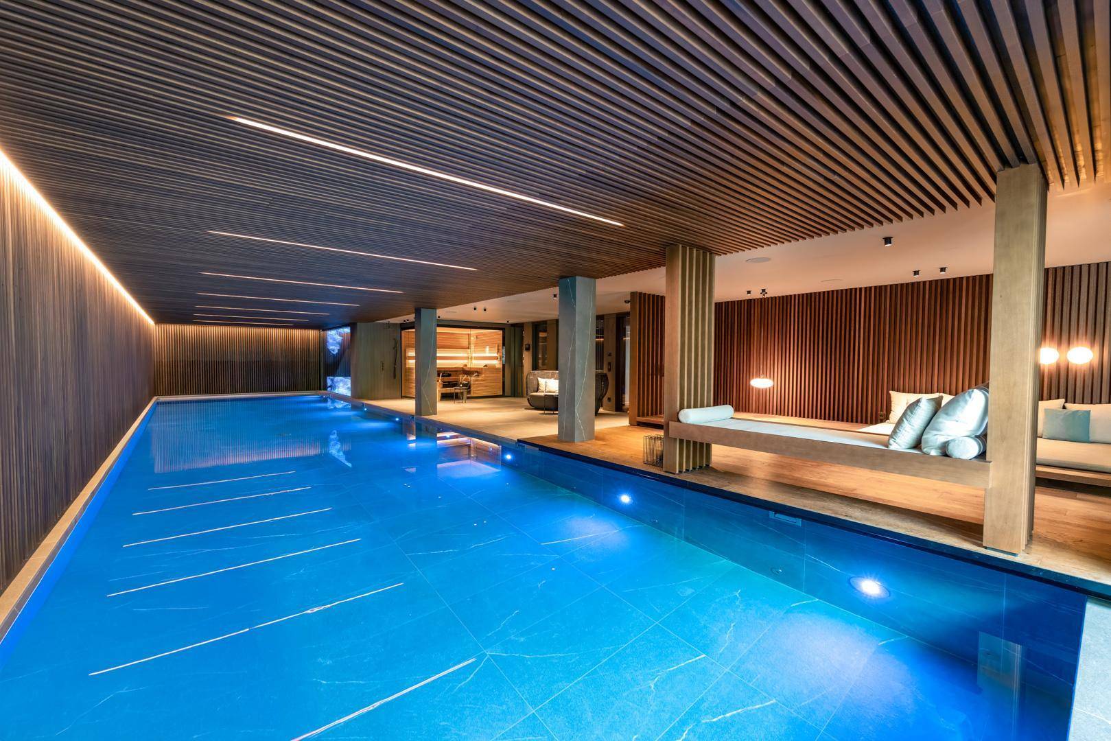Elegantes Hallenbad mit blauen Fliesen, Holzverkleidung und einem entspannenden Liegebereich.