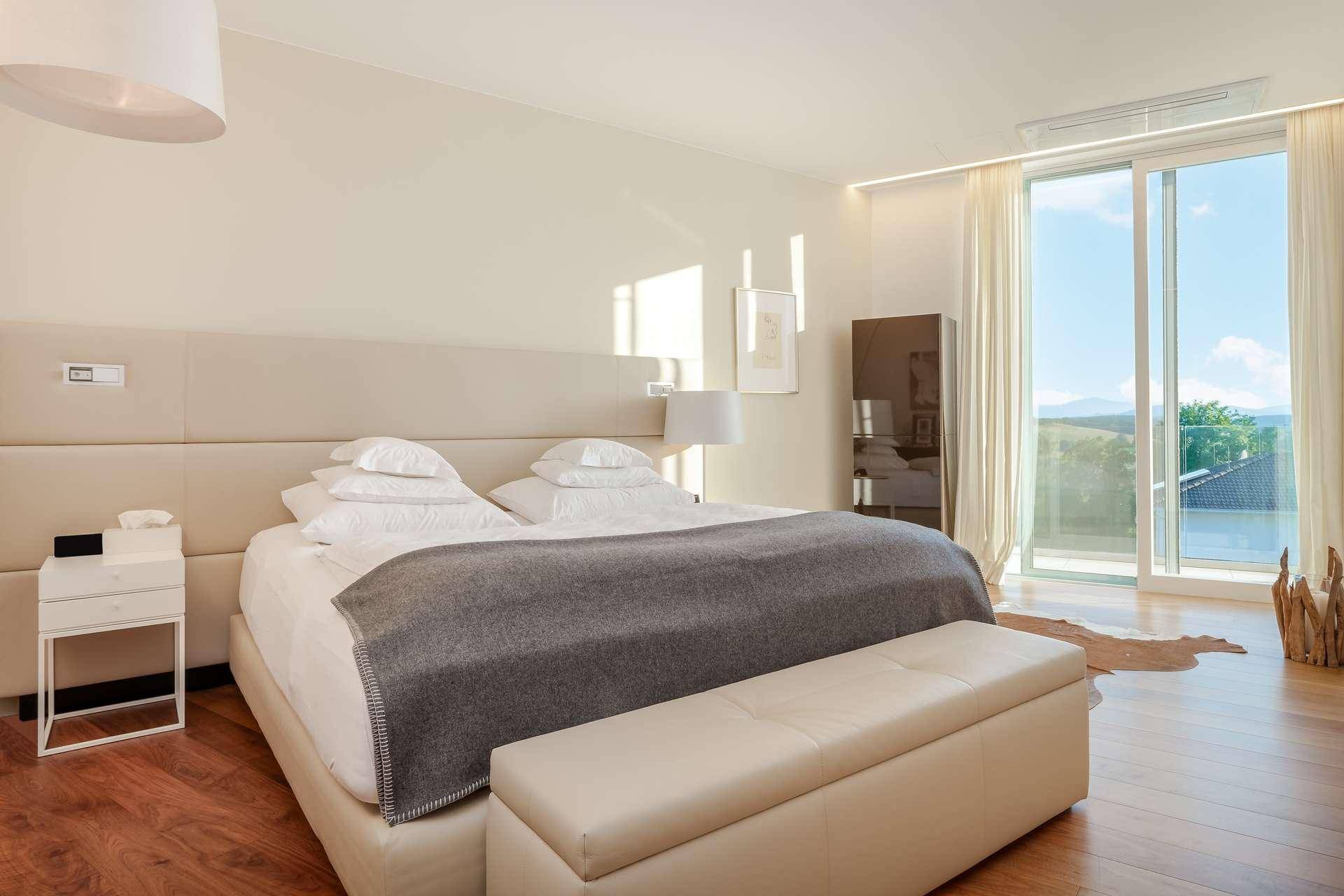 Helles Schlafzimmer mit großem Bett, Holzboden und Zugang zu einem Balkon mit Weitblick.