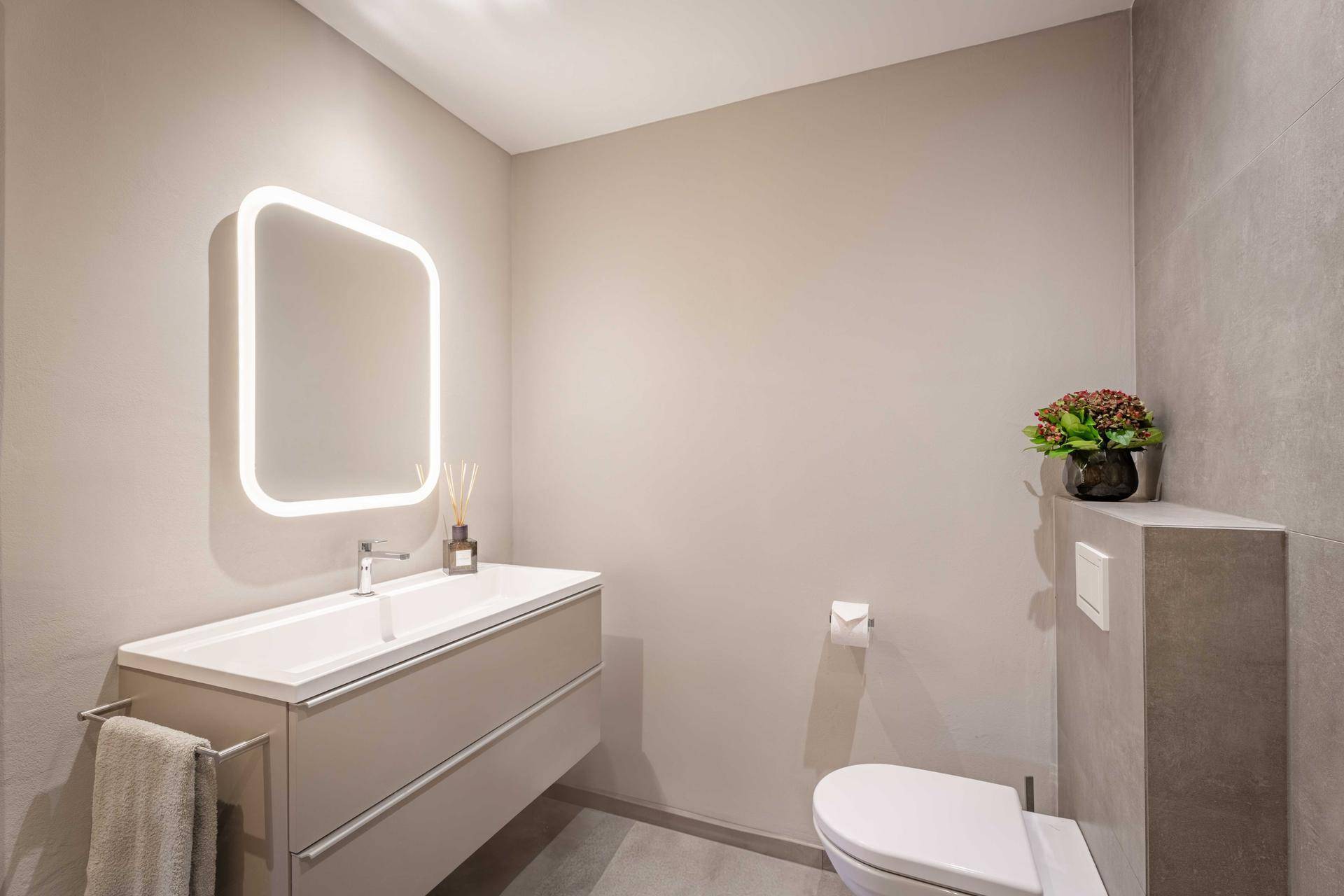 Modernes Badezimmer mit beleuchtetem Spiegel, Waschtisch und Wand-WC.