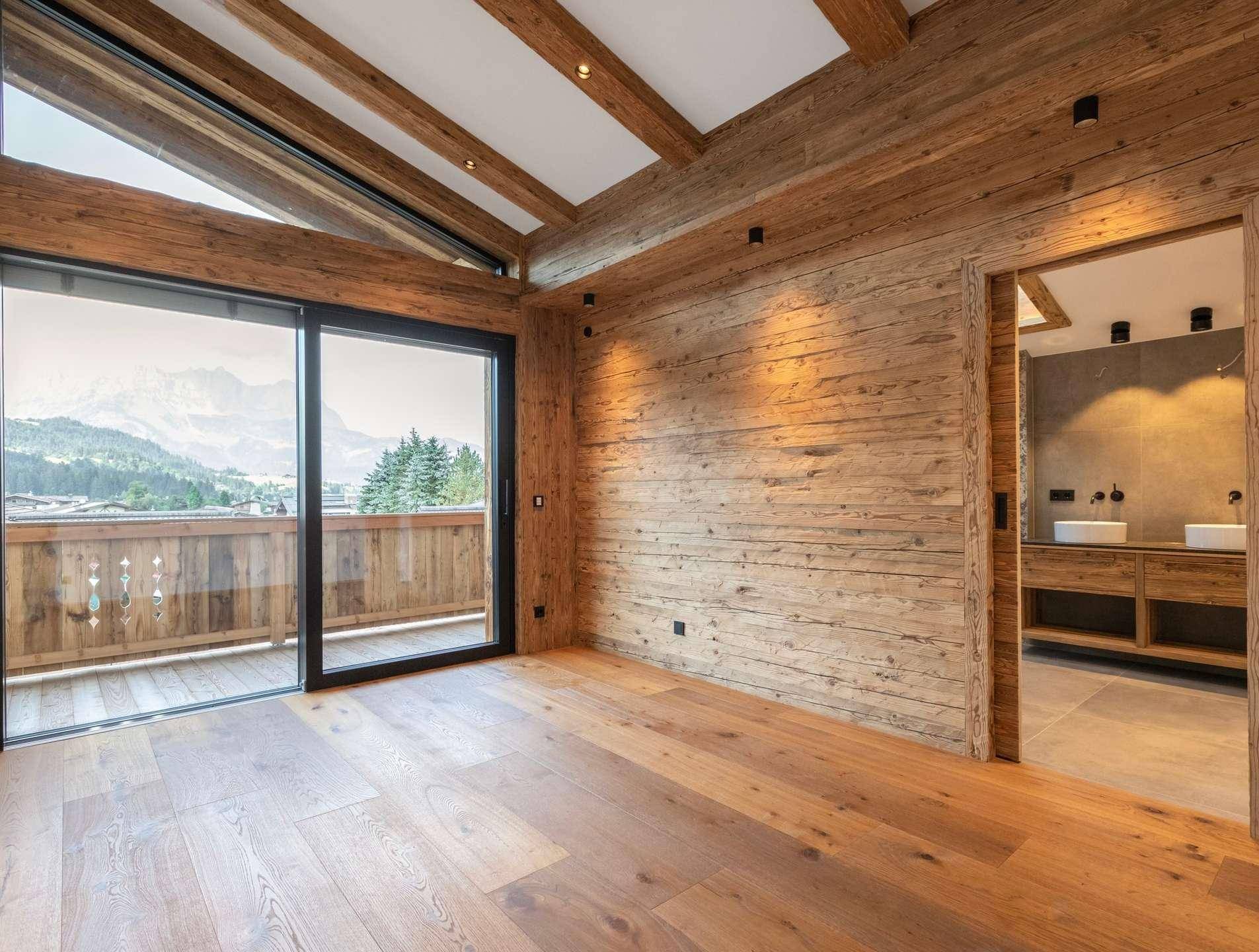 Gemütliches Schlafzimmer mit Holzwänden, Balkonzugang und Blick auf die umliegende Berglandschaft.