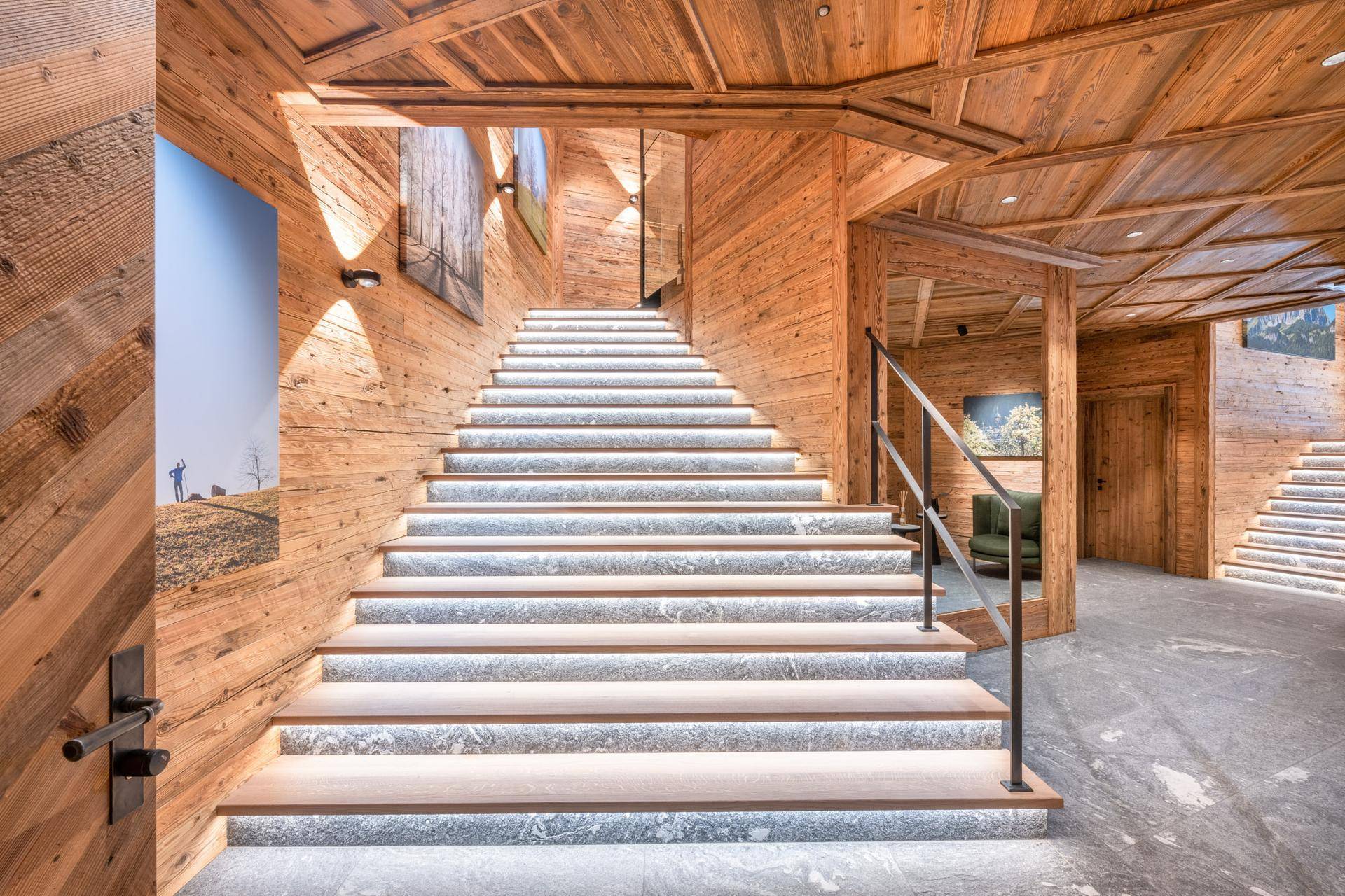 Beleuchtete Holztreppe mit Steinstufen und modernem Geländer, umgeben von Holzvertäfelung.