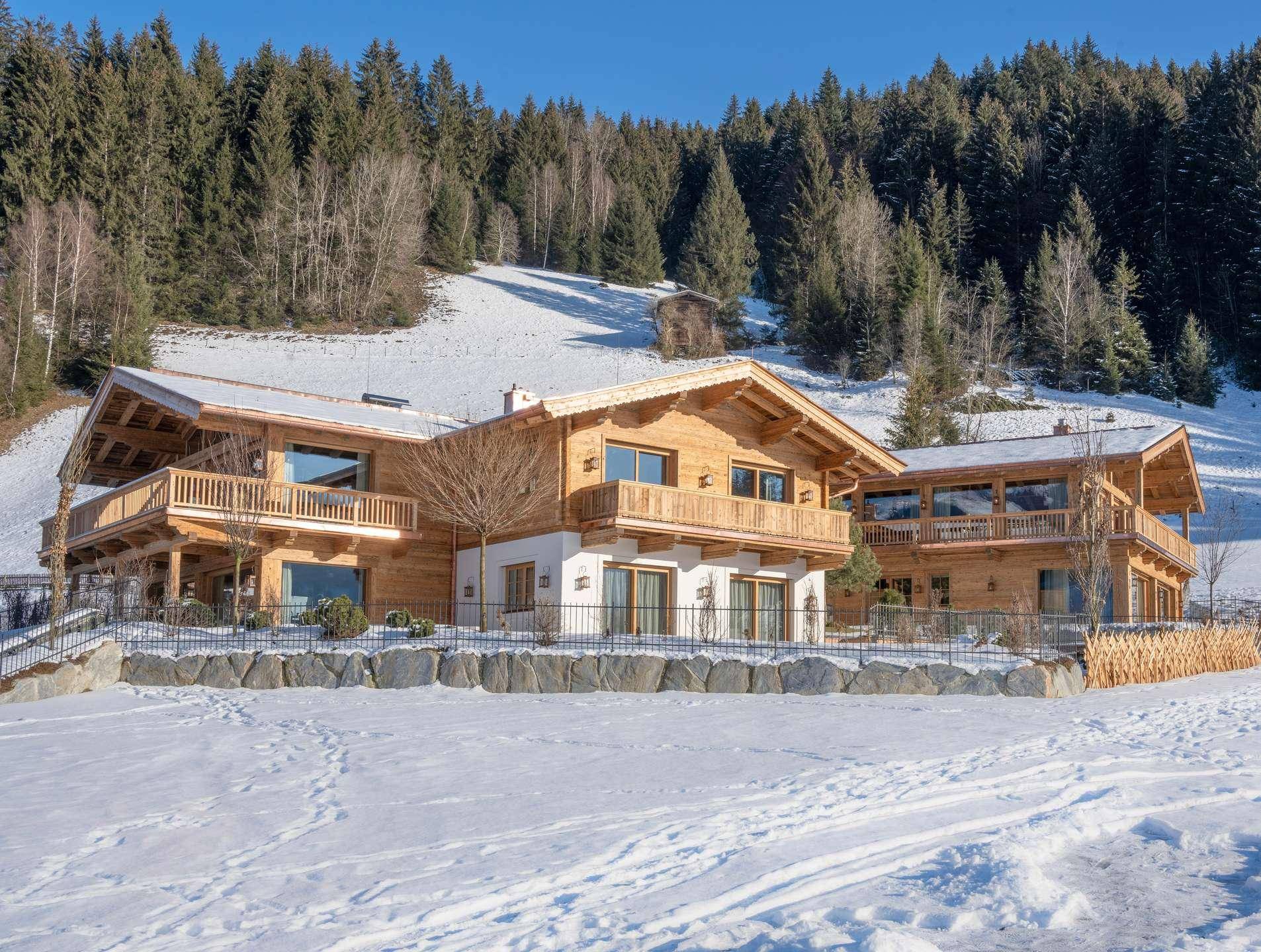 Beeindruckendes Holzchalet in verschneiter Berglandschaft, umgeben von Tannenbäumen unter blauem Himmel.