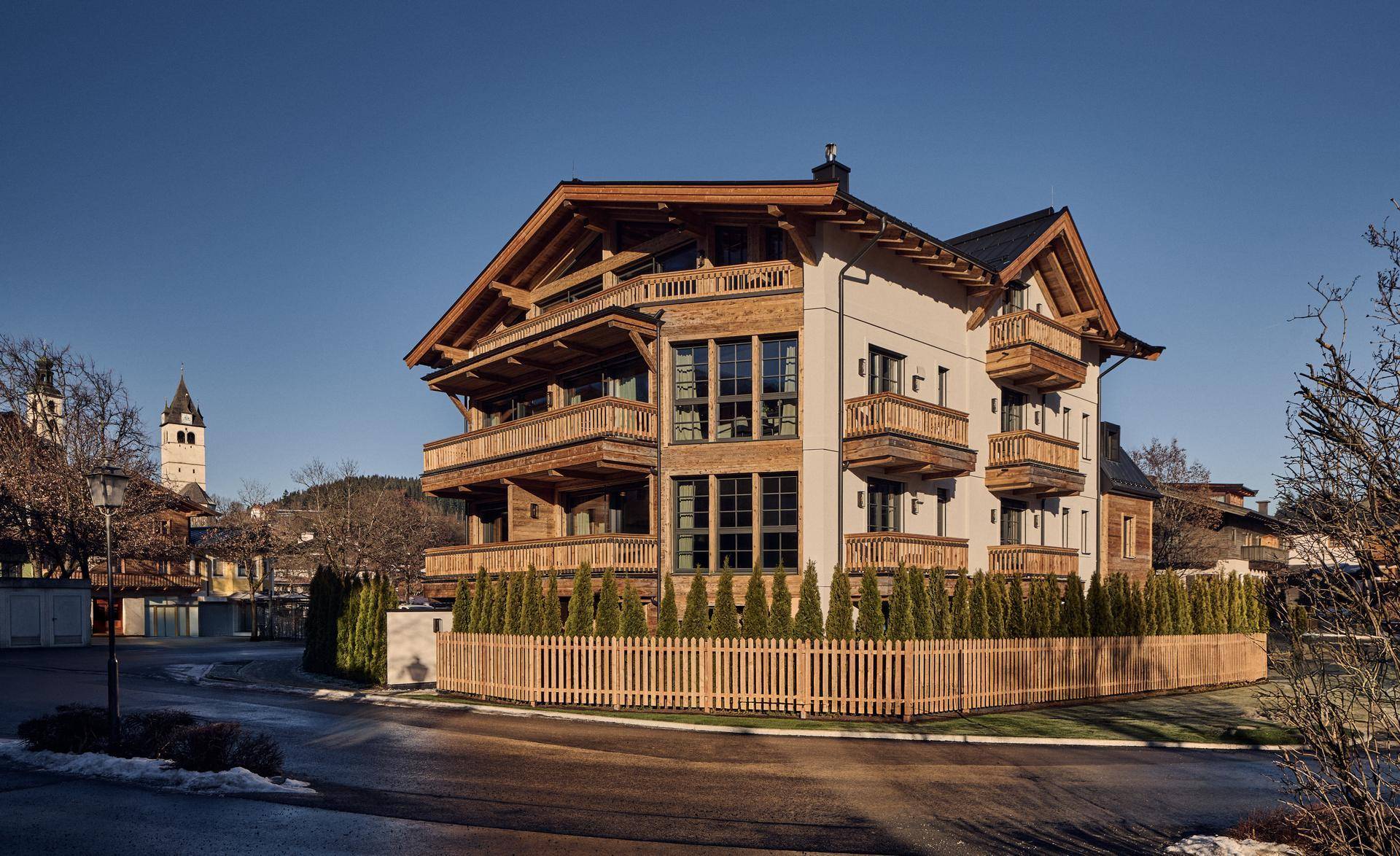 Modernes Chalet-Gebäude mit Holzfassade, vielen Balkonen und Satteldach in alpiner Umgebung.