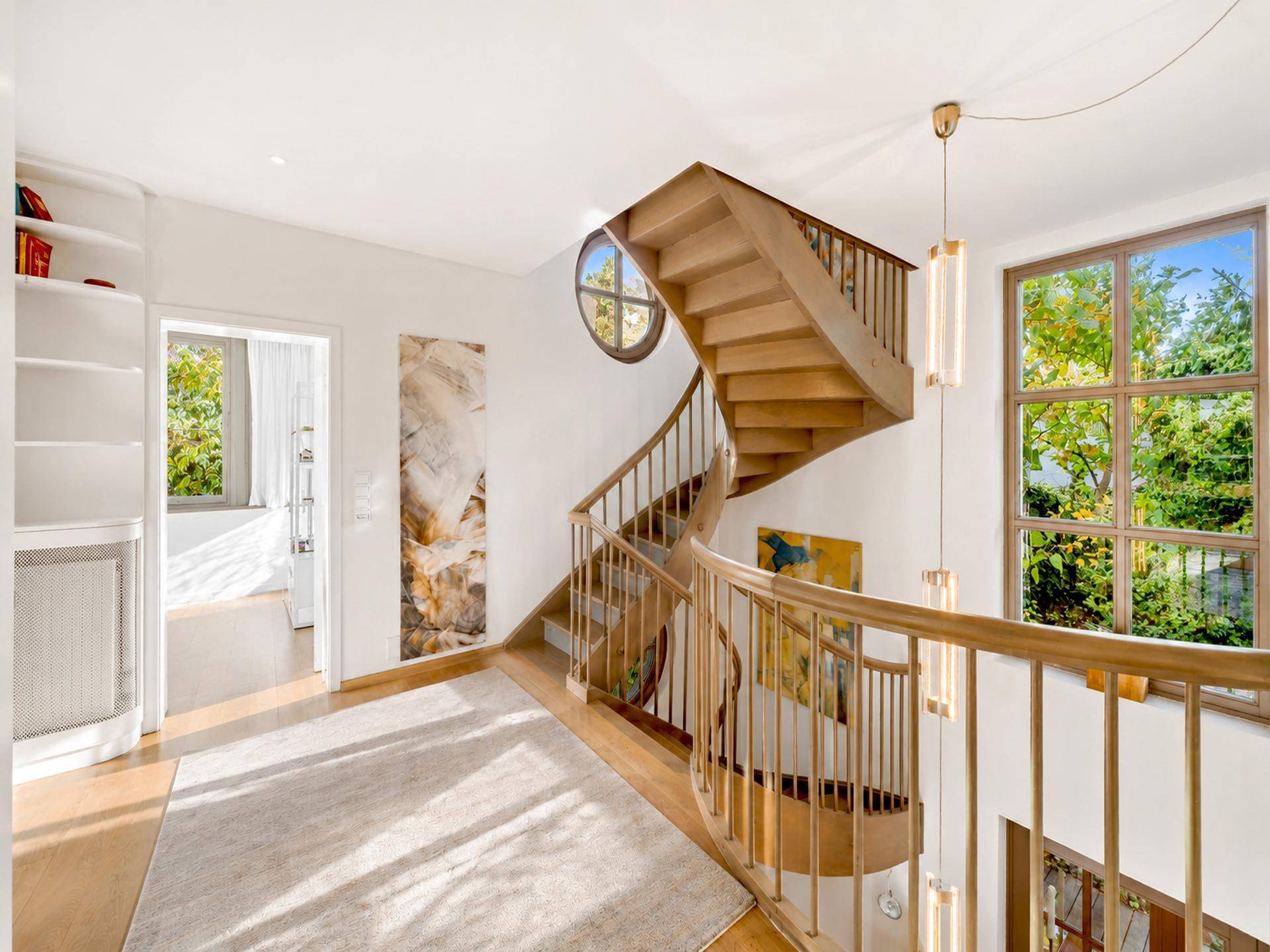 Lichtdurchfluteter Flur mit eleganter Holzwendeltreppe und hohen Fenstern, die viel Tageslicht hereinlassen.