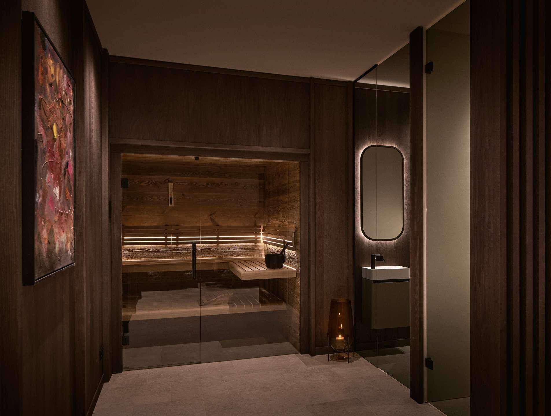 Exklusiver Wellnessbereich mit moderner Sauna und angrenzendem Waschbecken in dunklem Holzdesign.