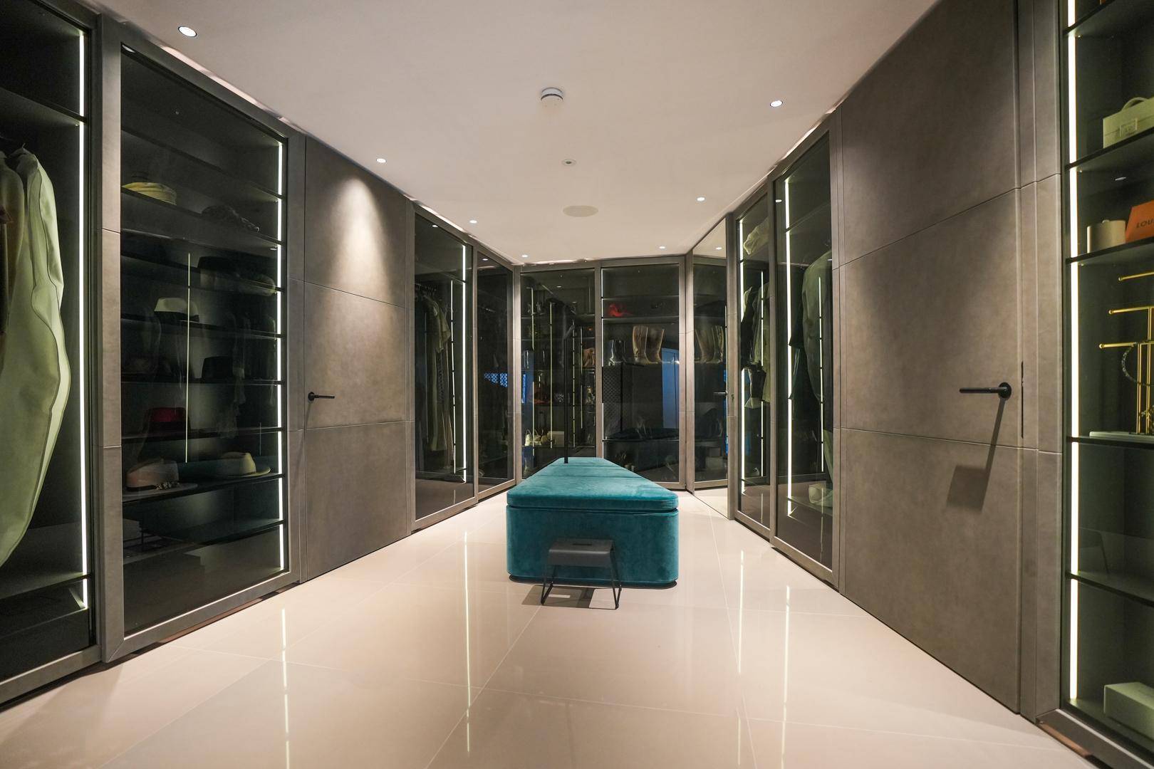 Luxuriöser begehbarer Kleiderschrank mit integrierter Beleuchtung, Glasfronten und viel Stauraum.