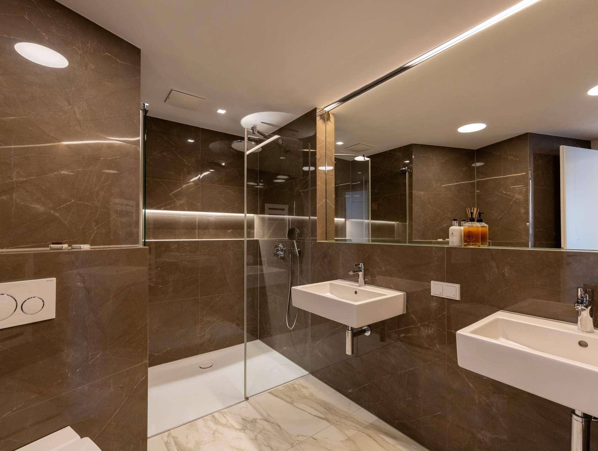 Luxuriöses Badezimmer mit doppelten Waschbecken, begehbarer Dusche und eleganten Marmorfliesen.