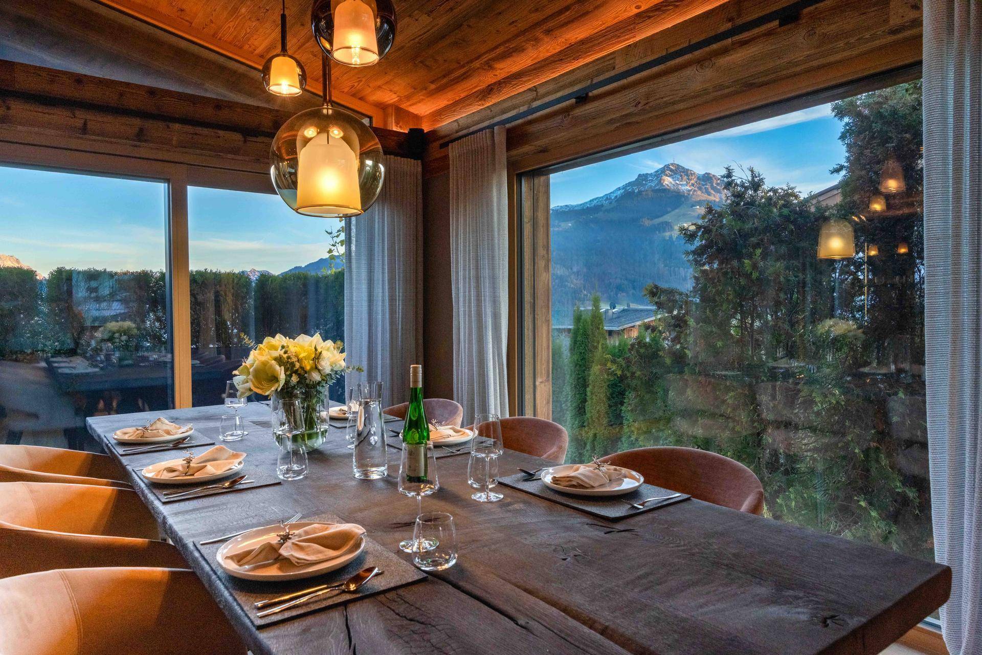 Stilvoller Essbereich mit Holztisch und beeindruckendem Blick auf die majestätischen Berge und grüne Natur.