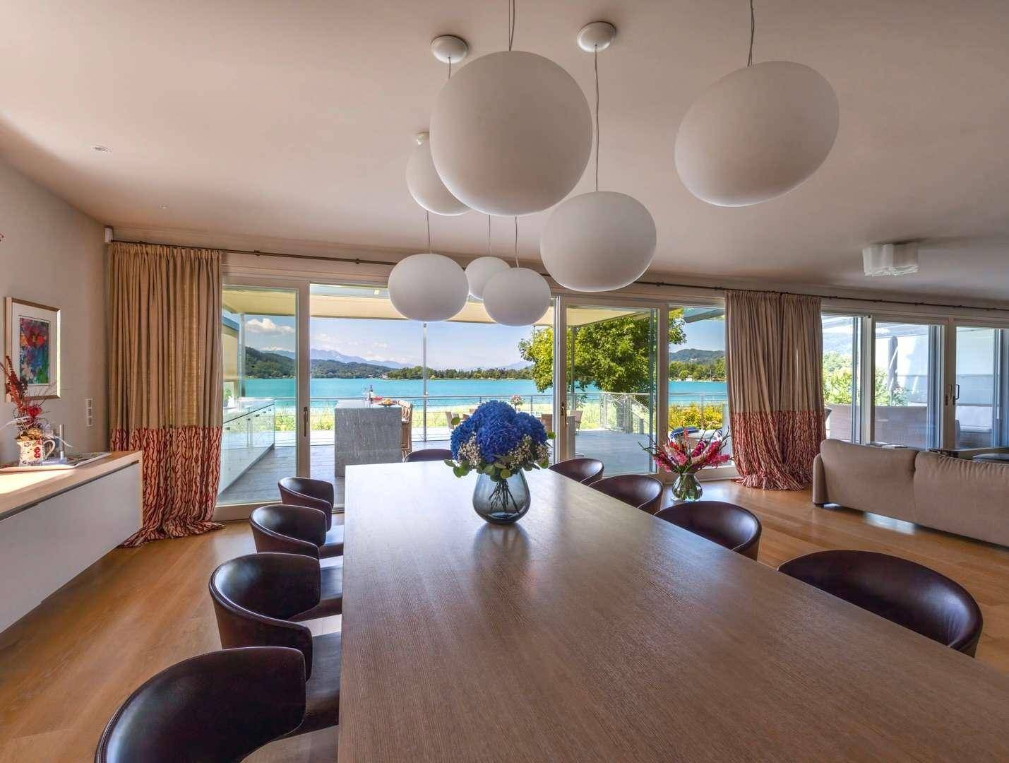Eleganter Essbereich mit Holztisch, modernen Hängelampen und weitem Blick auf den See.