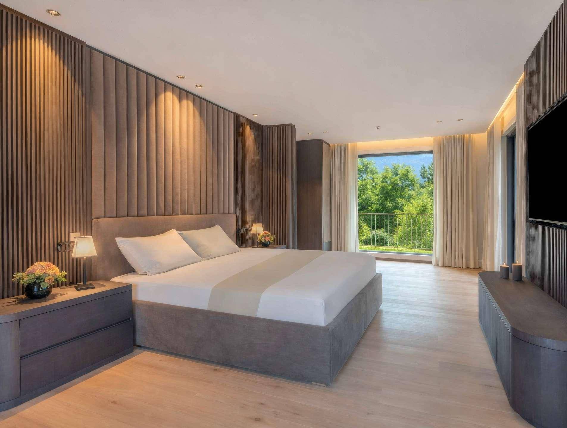 Modernes Schlafzimmer mit gepolsterter Wand, Holzboden und Zugang zu einem Balkon.