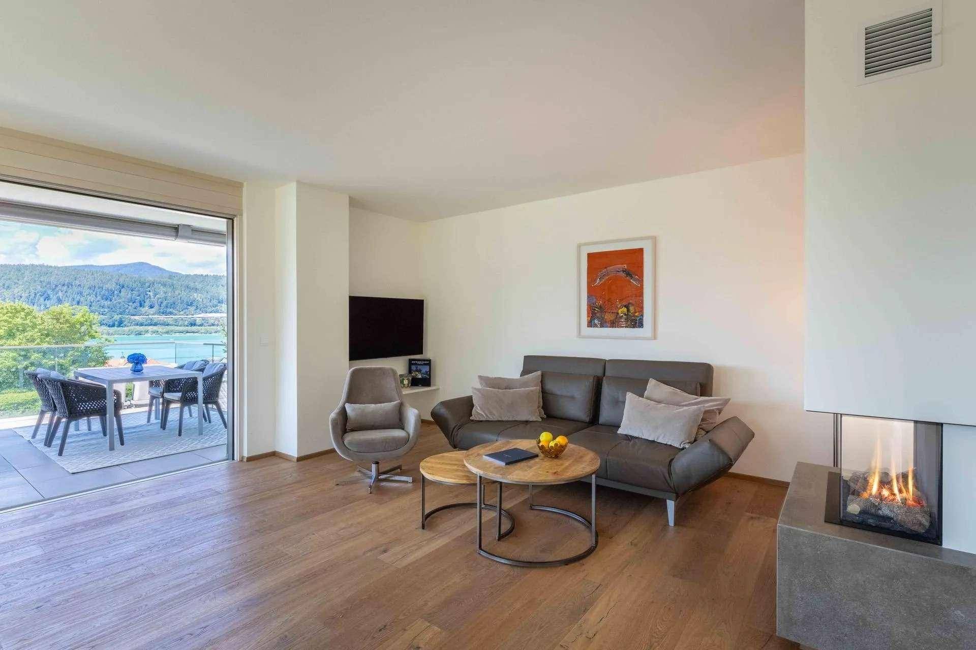 Gemütliches Wohnzimmer mit Kamin, Holzboden und Schiebetüren zur Terrasse mit Seeblick.