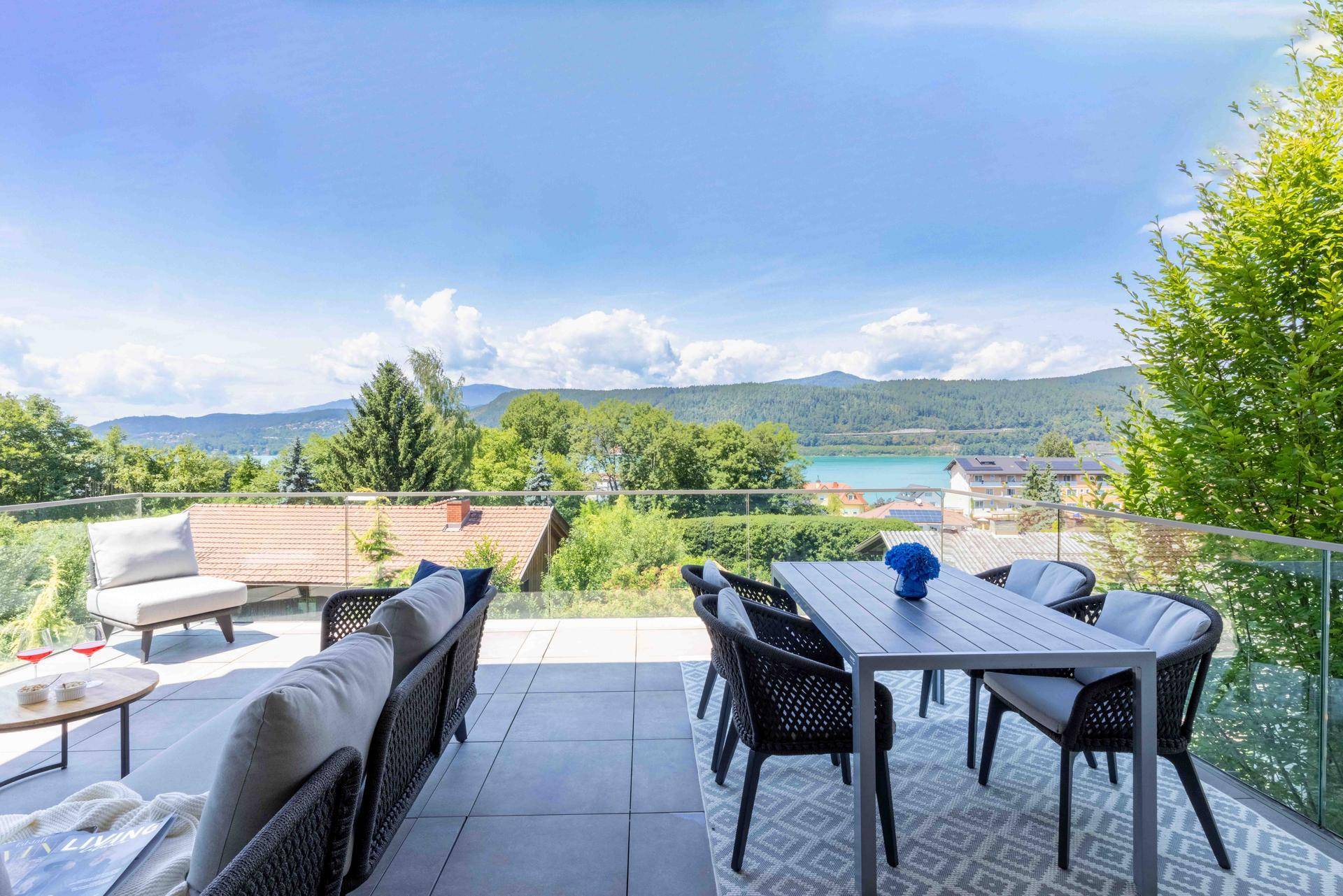 Große Sonnenterrasse mit modernen Gartenmöbeln und Panoramablick auf den See und die umliegende Landschaft.