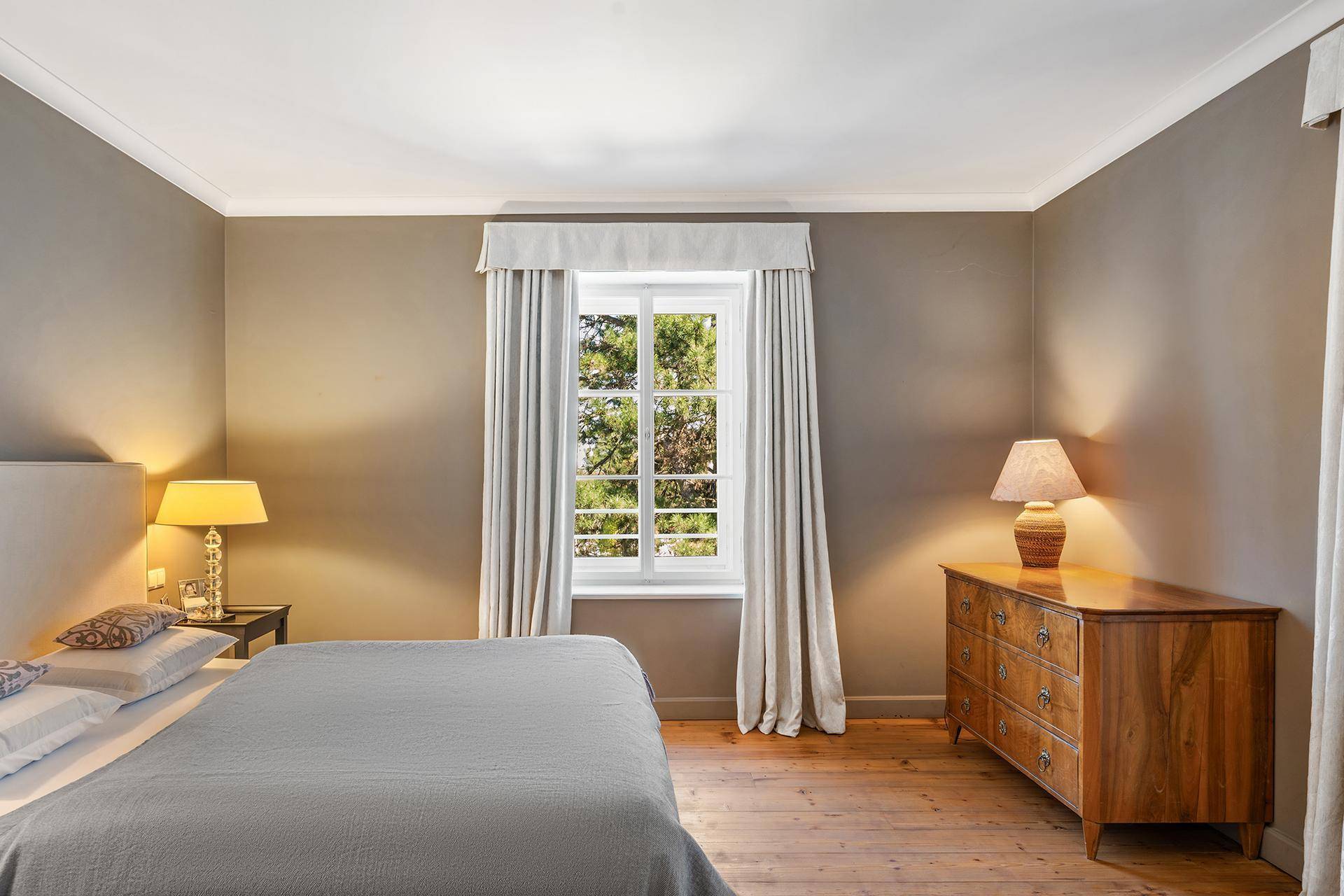 Gemütliches Schlafzimmer mit Holzboden, großem Bett und Fenster mit Blick ins Grüne.