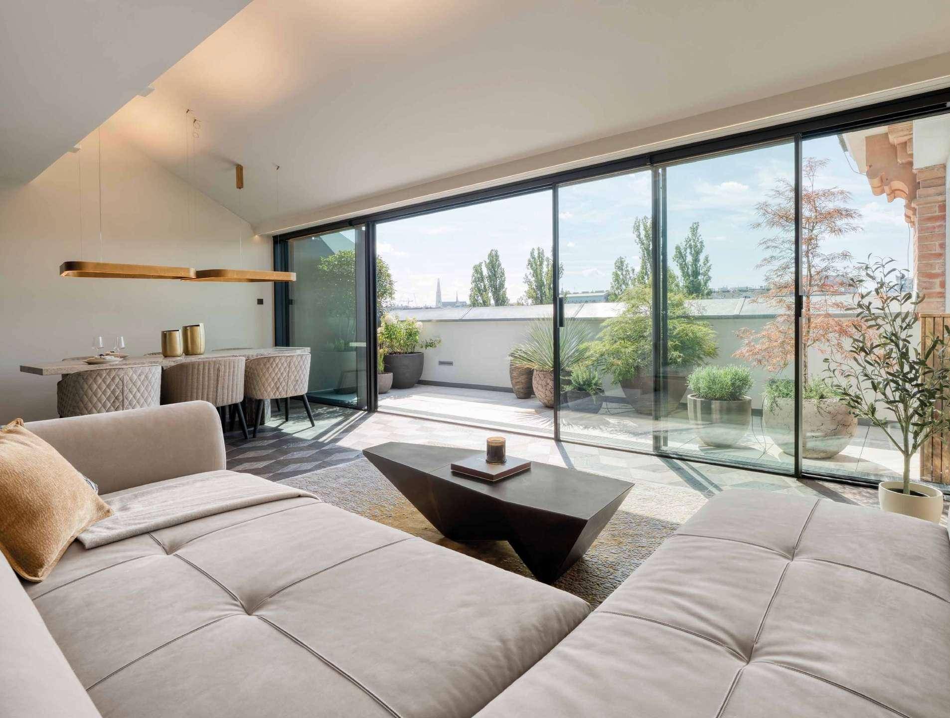 Helles Wohnzimmer mit großen Glasfronten und direktem Zugang zu einer Dachterrasse.