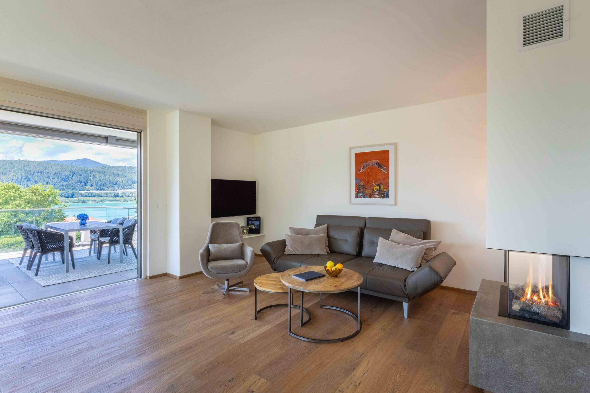 Gemütliches Wohnzimmer mit modernem Kamin, Holzboden und Zugang zu einer Terrasse mit Seeblick.