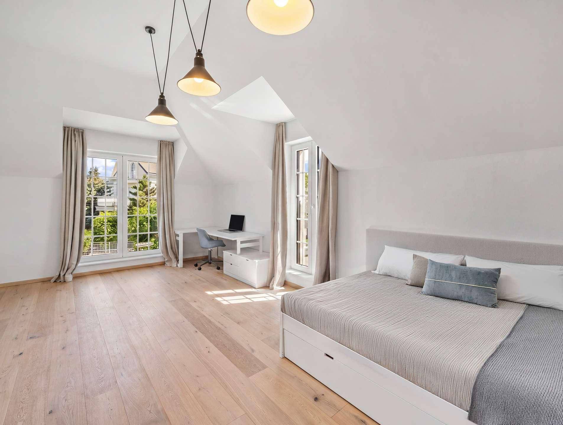 Helles Schlafzimmer im Dachgeschoss mit Holzboden, Schreibtisch und großen Fenstern.