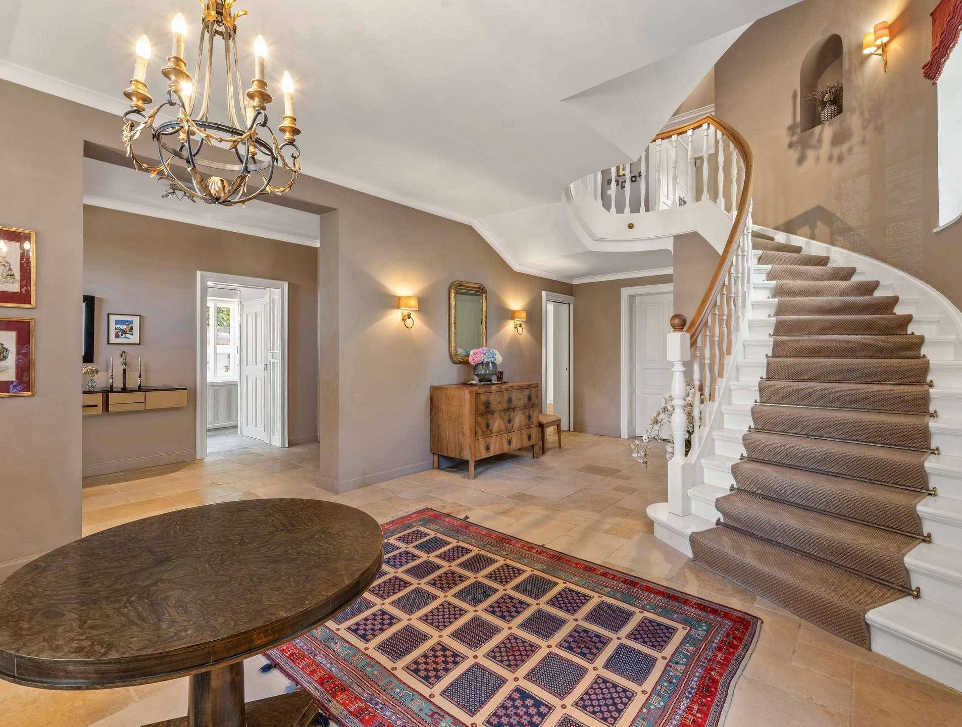 Geräumige Eingangshalle mit eleganter geschwungener Treppe, Fliesenboden und klassischer Einrichtung.