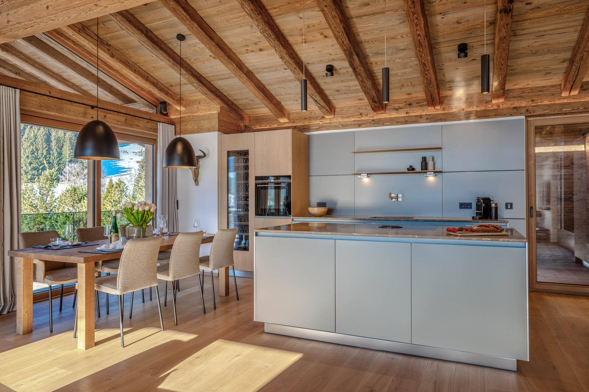 Elegante, moderne Küche mit Kochinsel, integrierten Geräten und Essbereich unter Holzbalken.