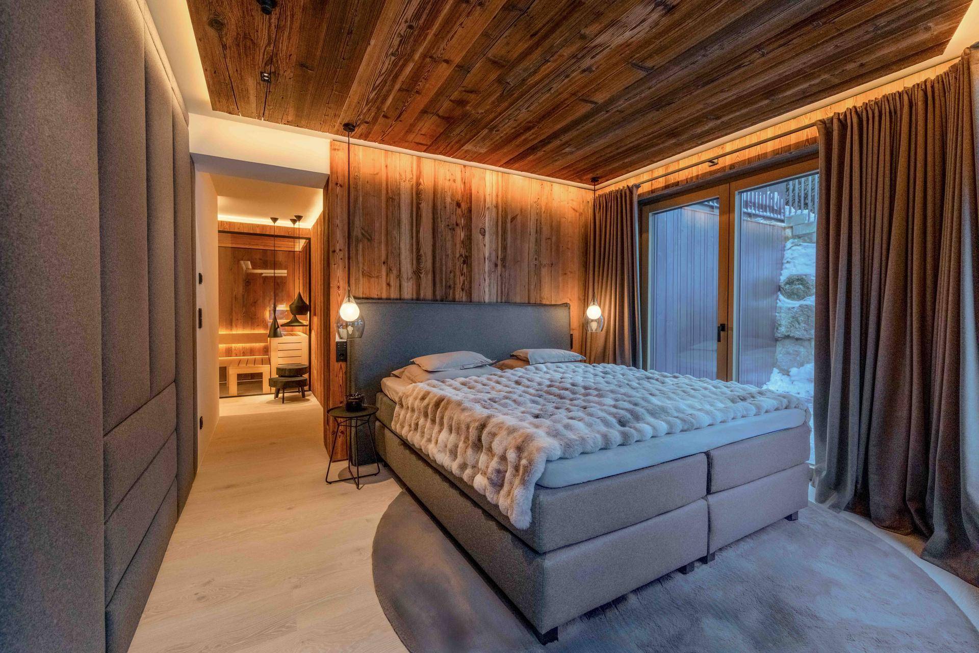 Schlafzimmer mit Holzwänden und -decke, großem Bett und Zugang zum Außenbereich.