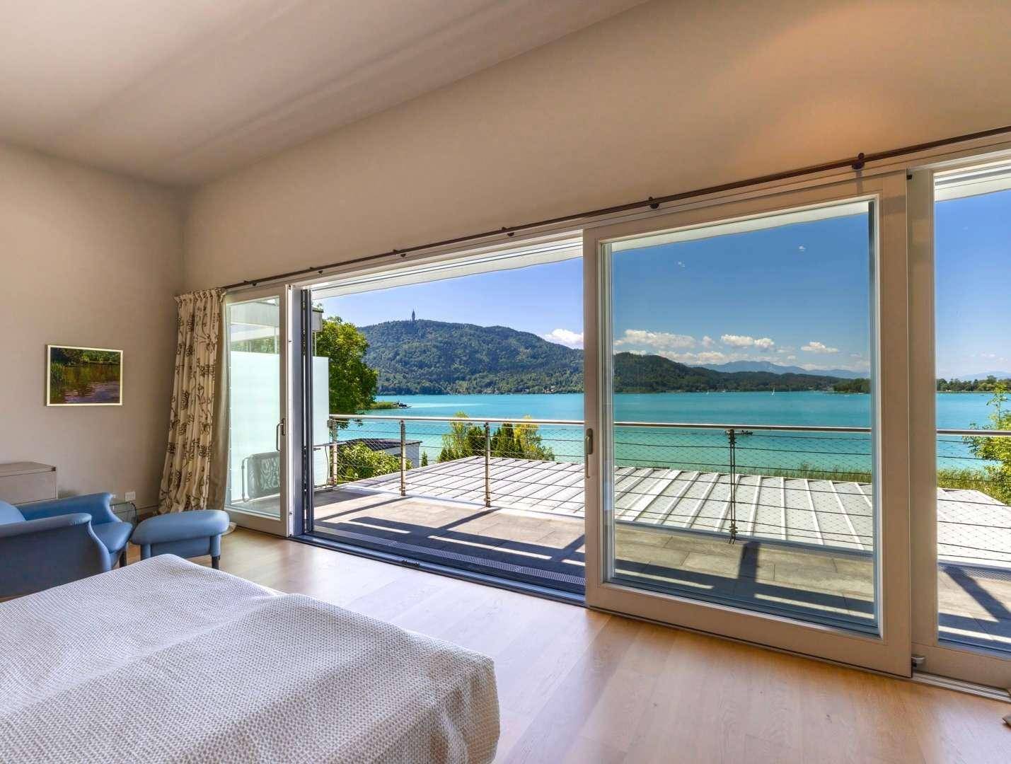 Helles Schlafzimmer mit Holzboden und Zugang zu einer Terrasse mit Panoramablick auf den See.