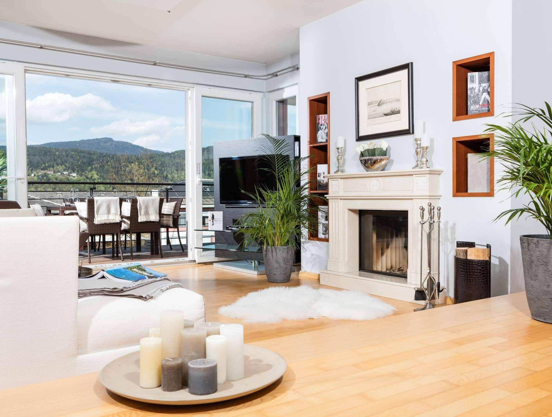 Gemütliches Wohnzimmer mit Kamin und großen Schiebetüren, die zu einem Balkon mit See- und Bergblick führen.
