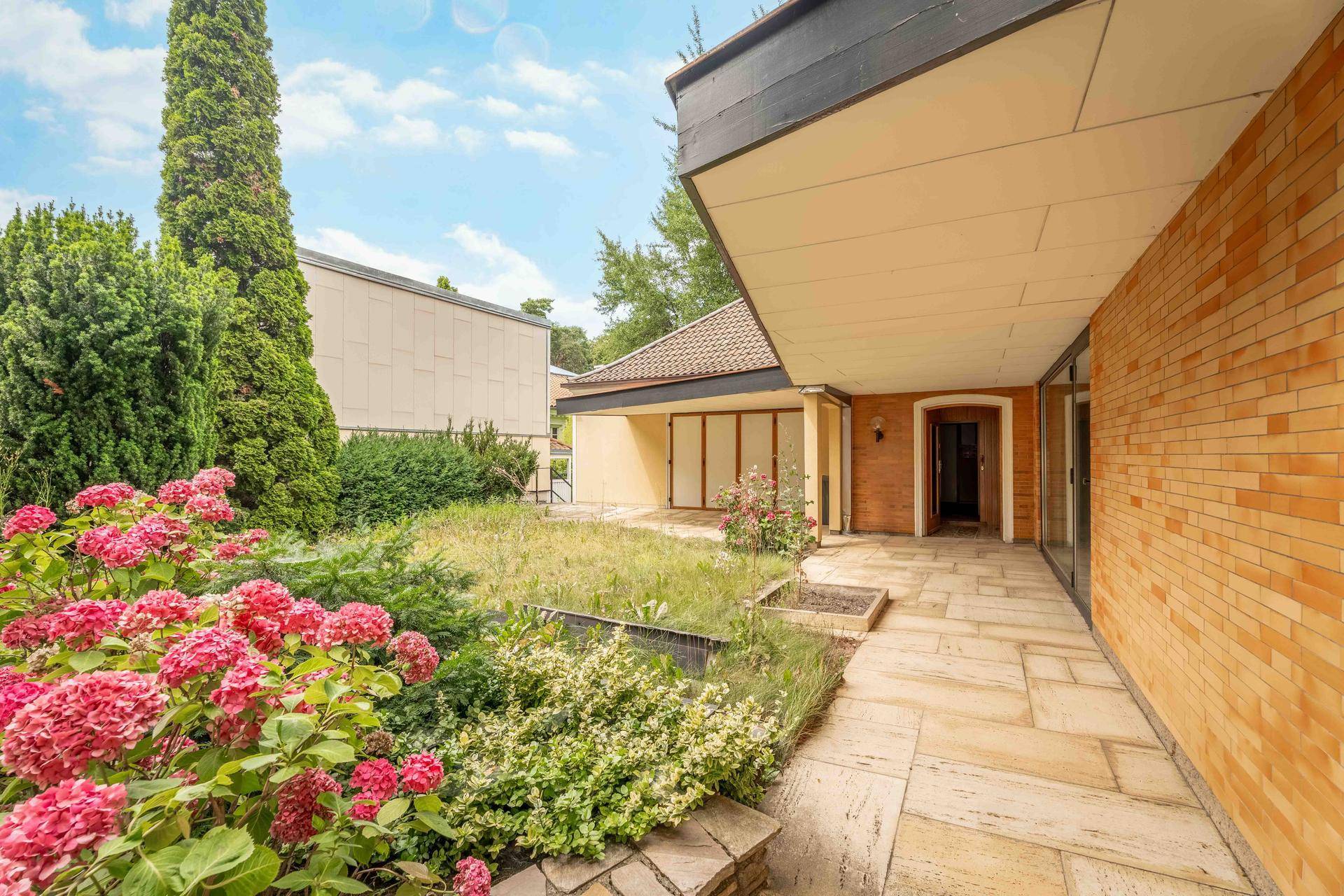 Gepflasterte Terrasse mit angrenzendem Garten und blühenden Hortensien vor dem Hauseingang.