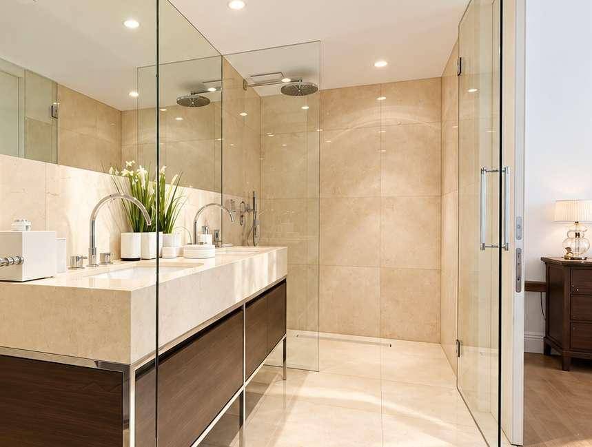 Modernes Badezimmer mit doppelten Waschbecken, begehbarer Glasdusche und beigefarbenen Fliesen.