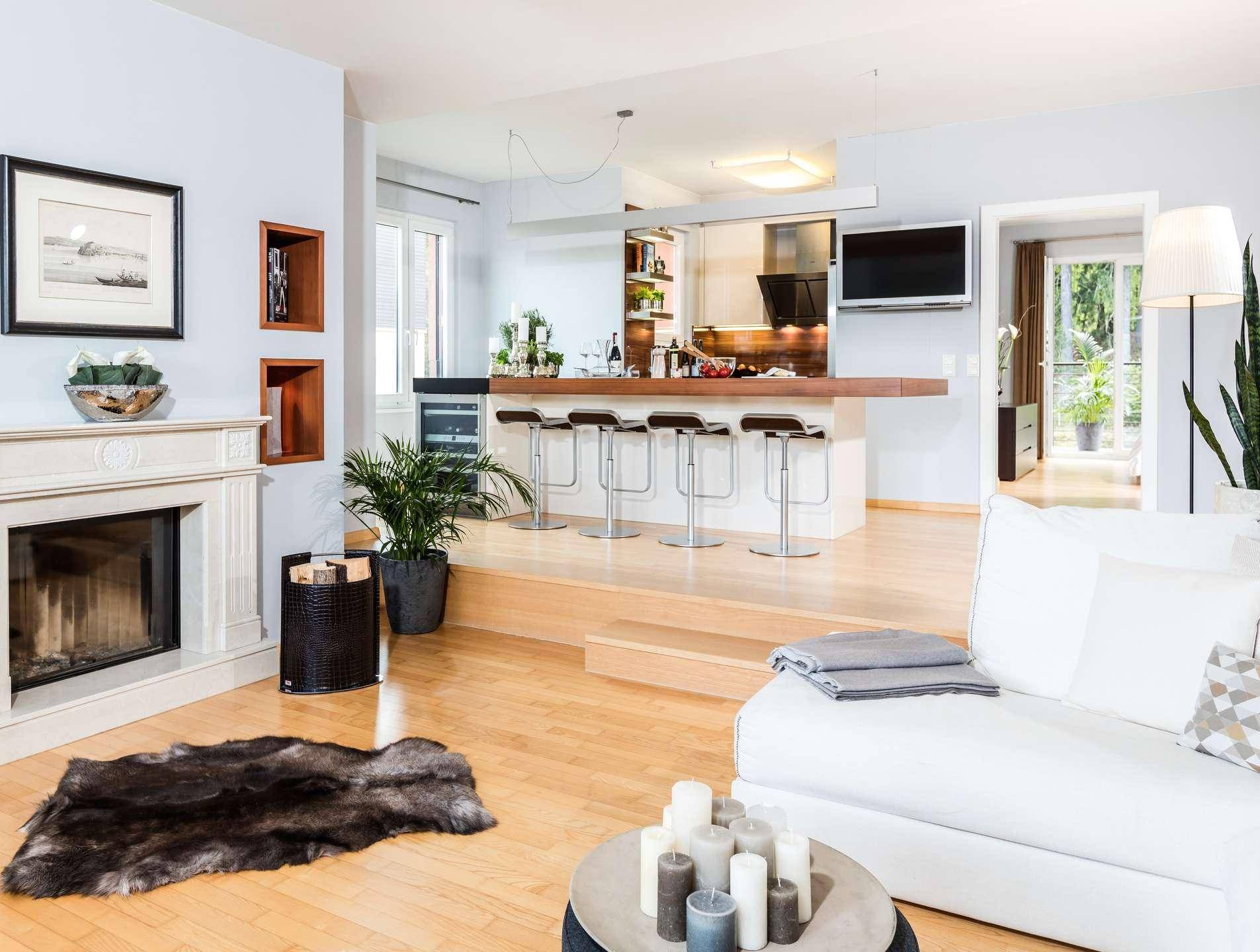 Heller offener Wohnbereich mit Kamin, weißem Sofa und erhöhter Bar-Küche mit Holzboden.