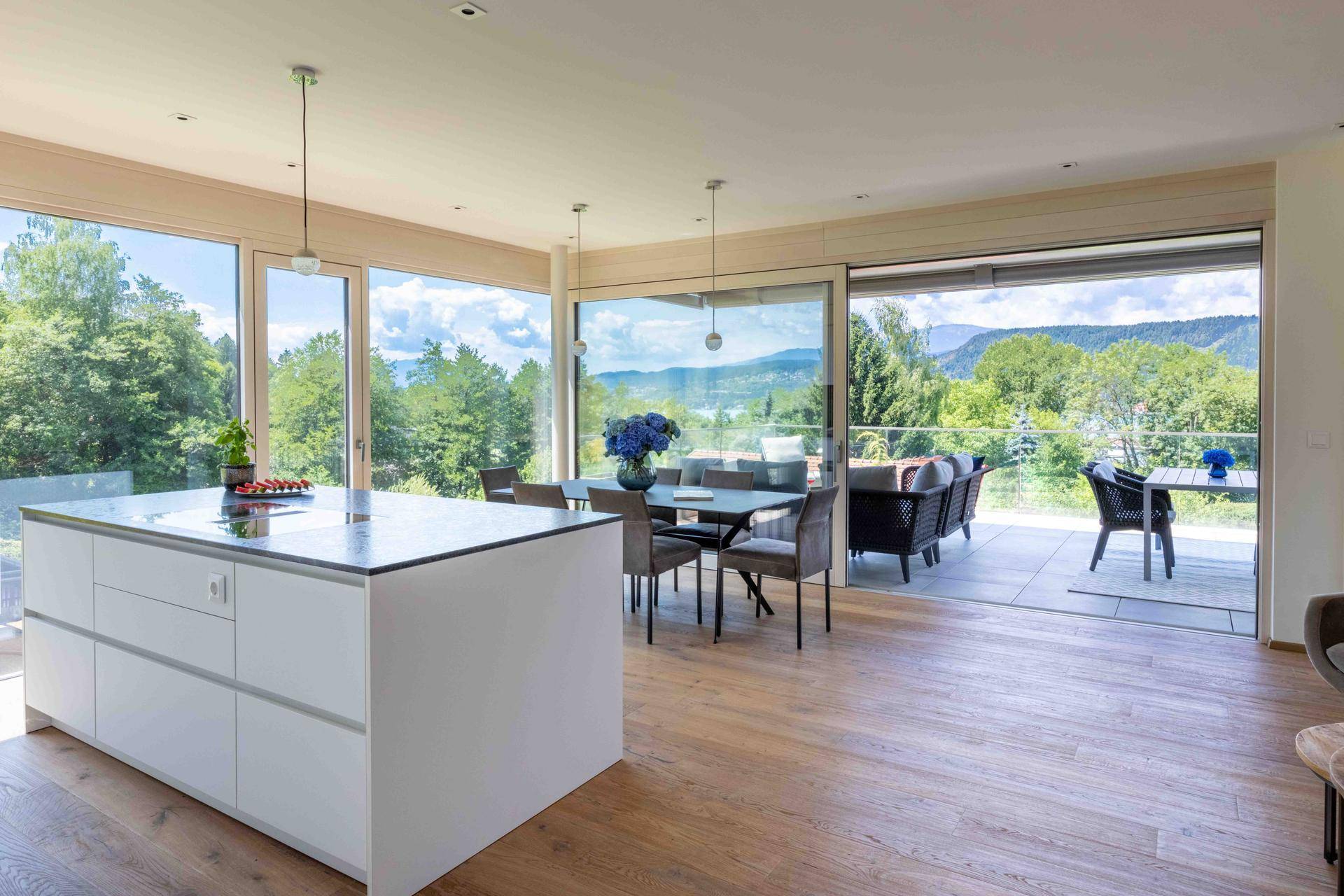Heller offener Wohn-Essbereich mit moderner Küche, Holzboden und großen Fenstern mit Seeblick.