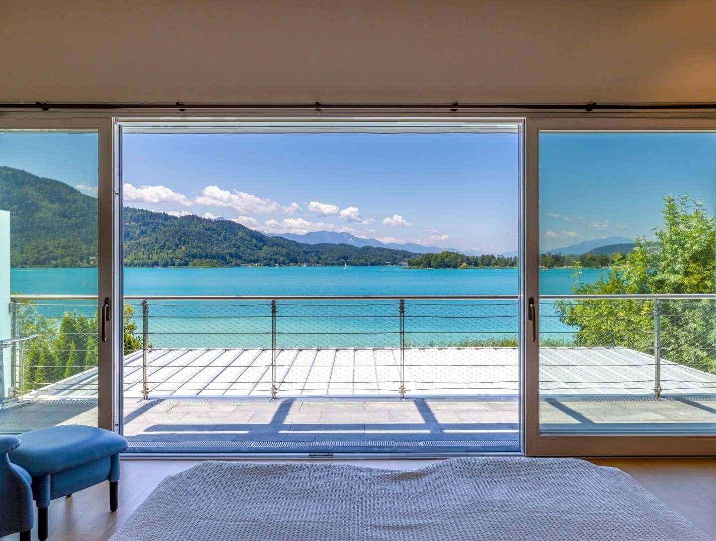 Schlafzimmer mit großen Schiebetüren, die einen spektakulären Blick auf den See und die umliegenden Berge bieten.