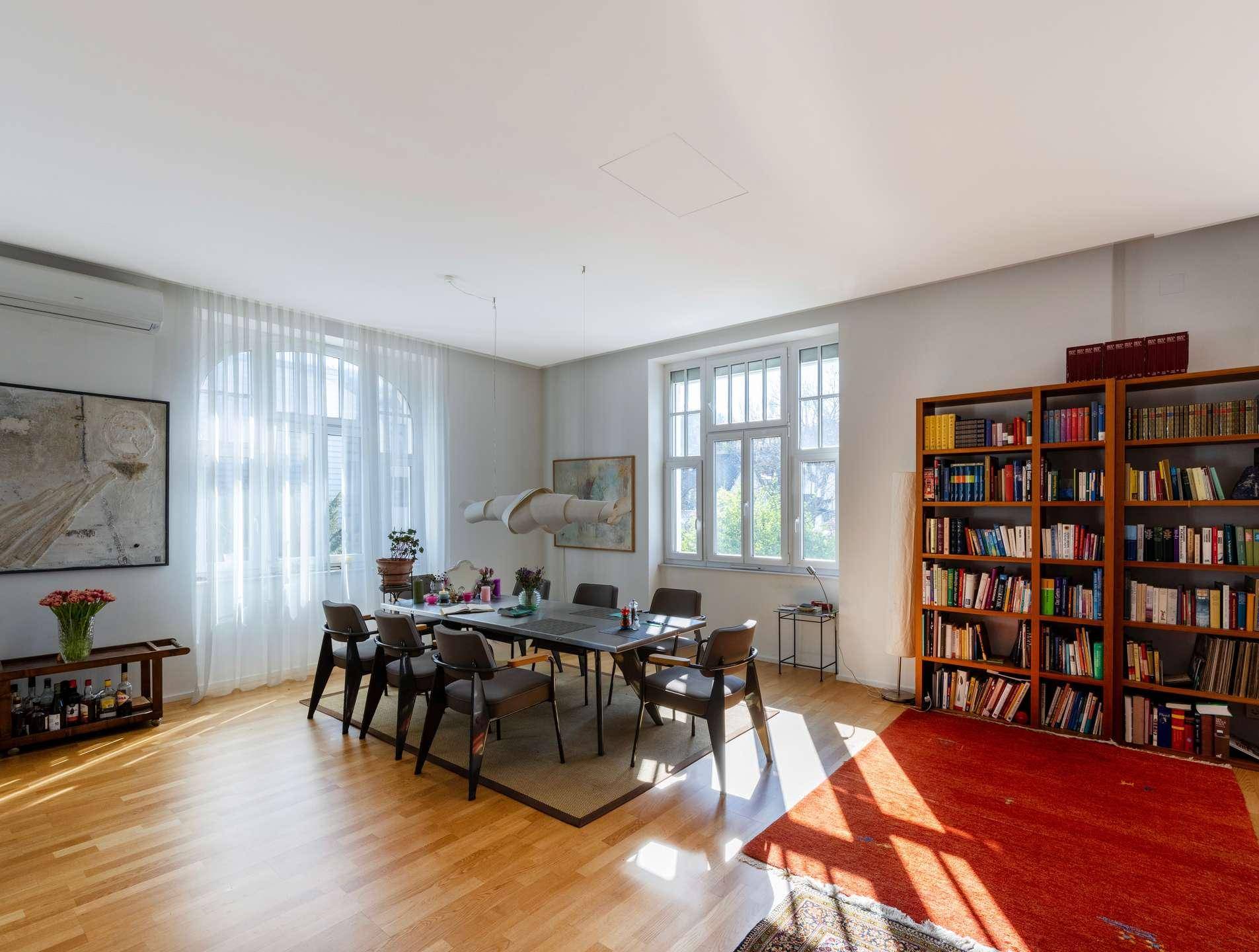 Geräumiger Essbereich mit Holzboden, großen Fenstern und einem Bücherregal.