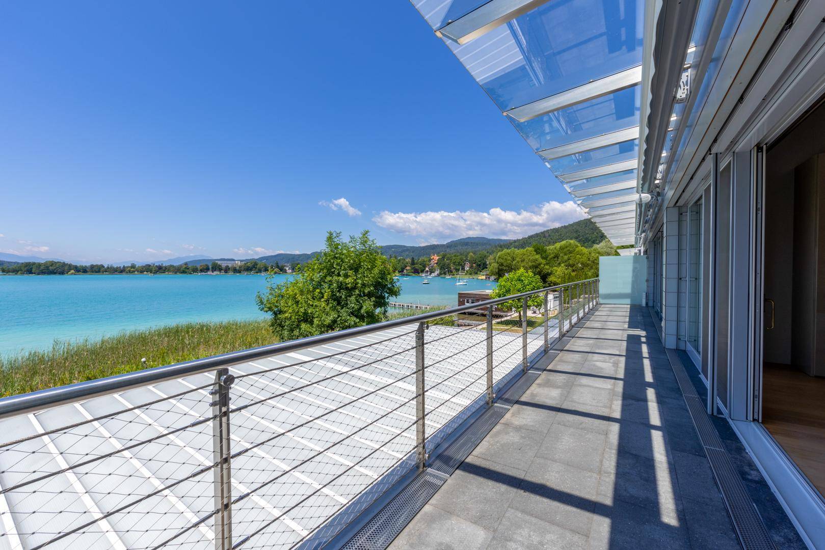 Langer Balkon mit Glasdach und Edelstahlgeländer, bietet einen weiten Blick über den See.