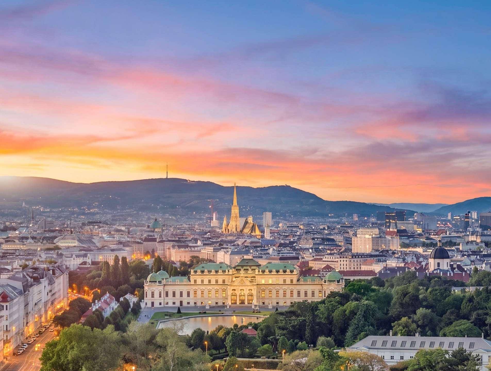 Panoramablick über Wien bei Sonnenuntergang mit dem Belvedere Palast und den umliegenden Bergen.