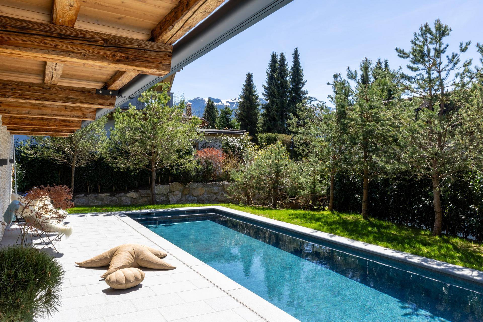Terrasse mit Pool und Bergblick, umgeben von grüner Natur und Bäumen.