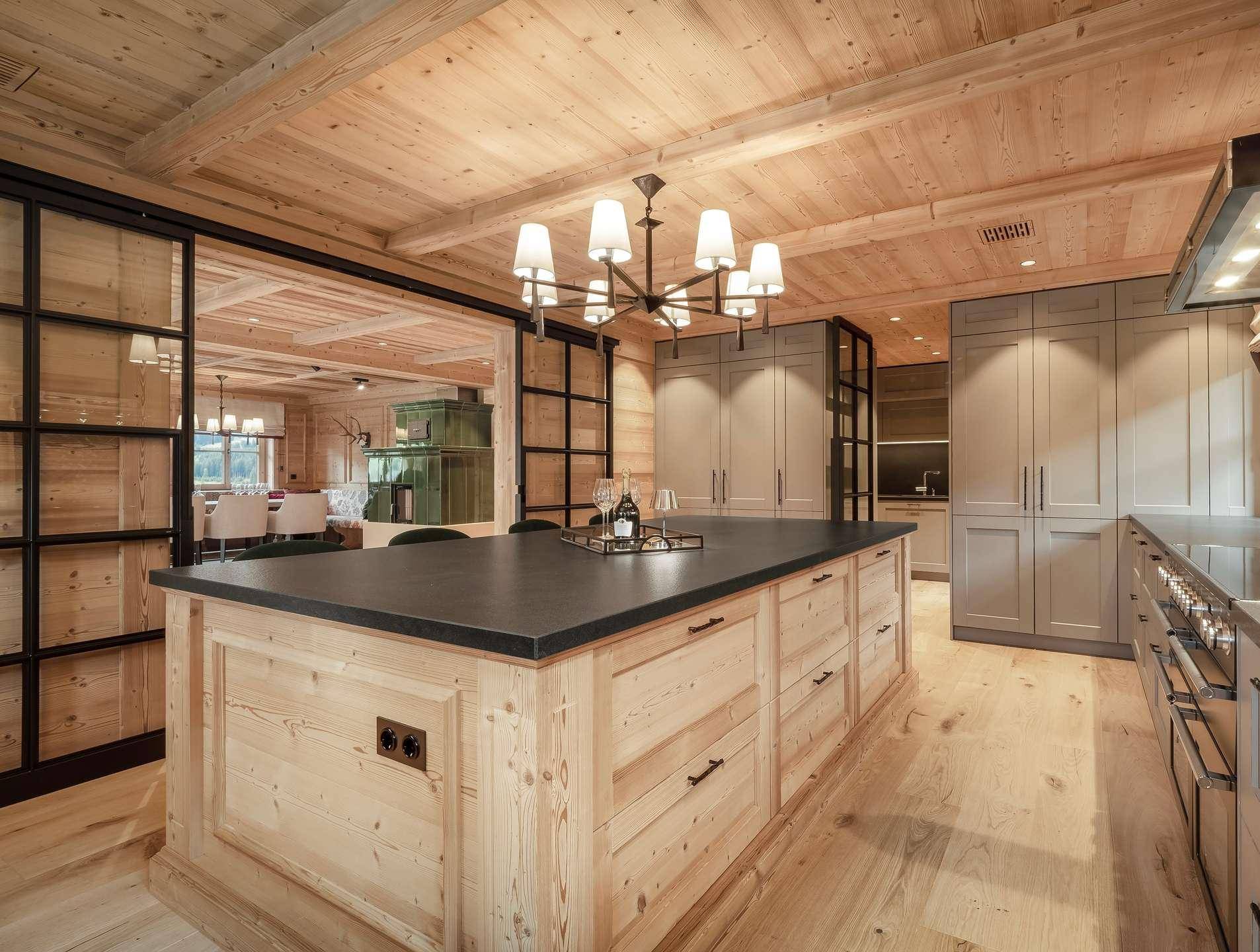 Moderne Holzküche mit großer Kochinsel, dunkler Arbeitsplatte und Glasabtrennung zum Essbereich.