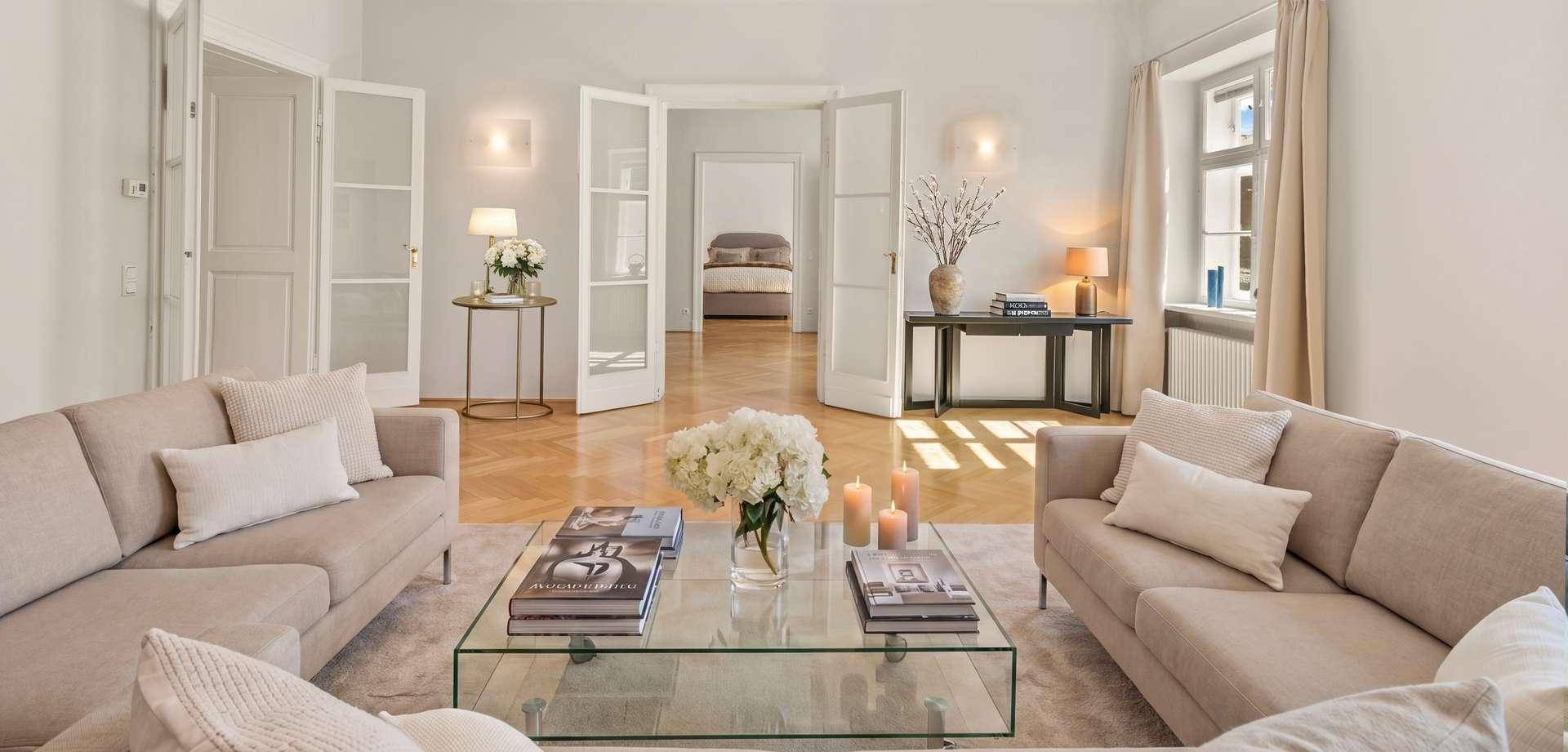 Helles Wohnzimmer mit eleganten Sofas, Parkettboden und Blick in ein Schlafzimmer.