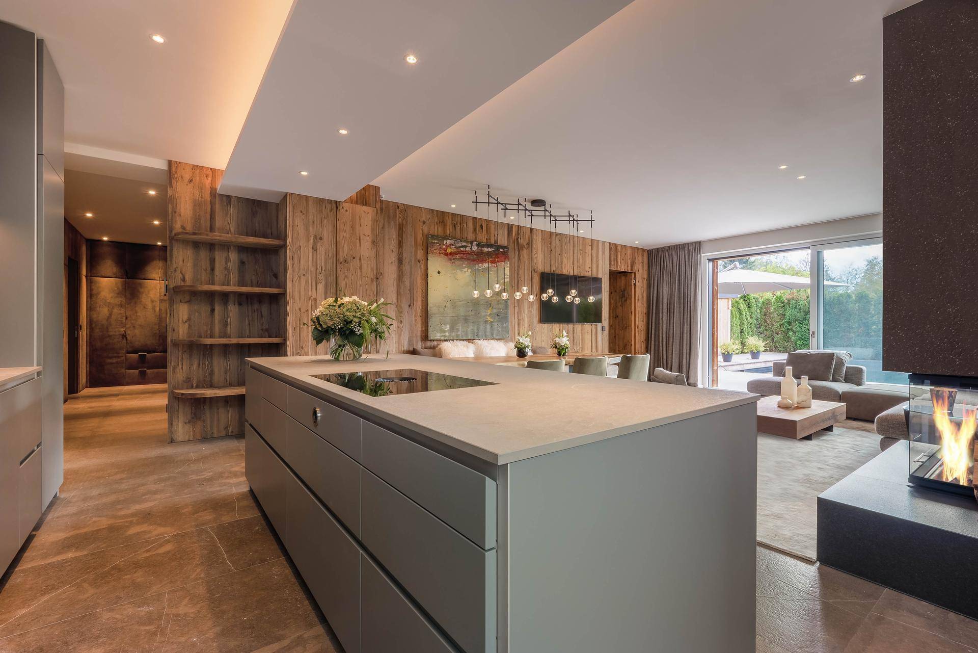 Offener Wohn- und Essbereich mit moderner Küche, Holzwänden und Kamin in einem luxuriösen Ambiente.