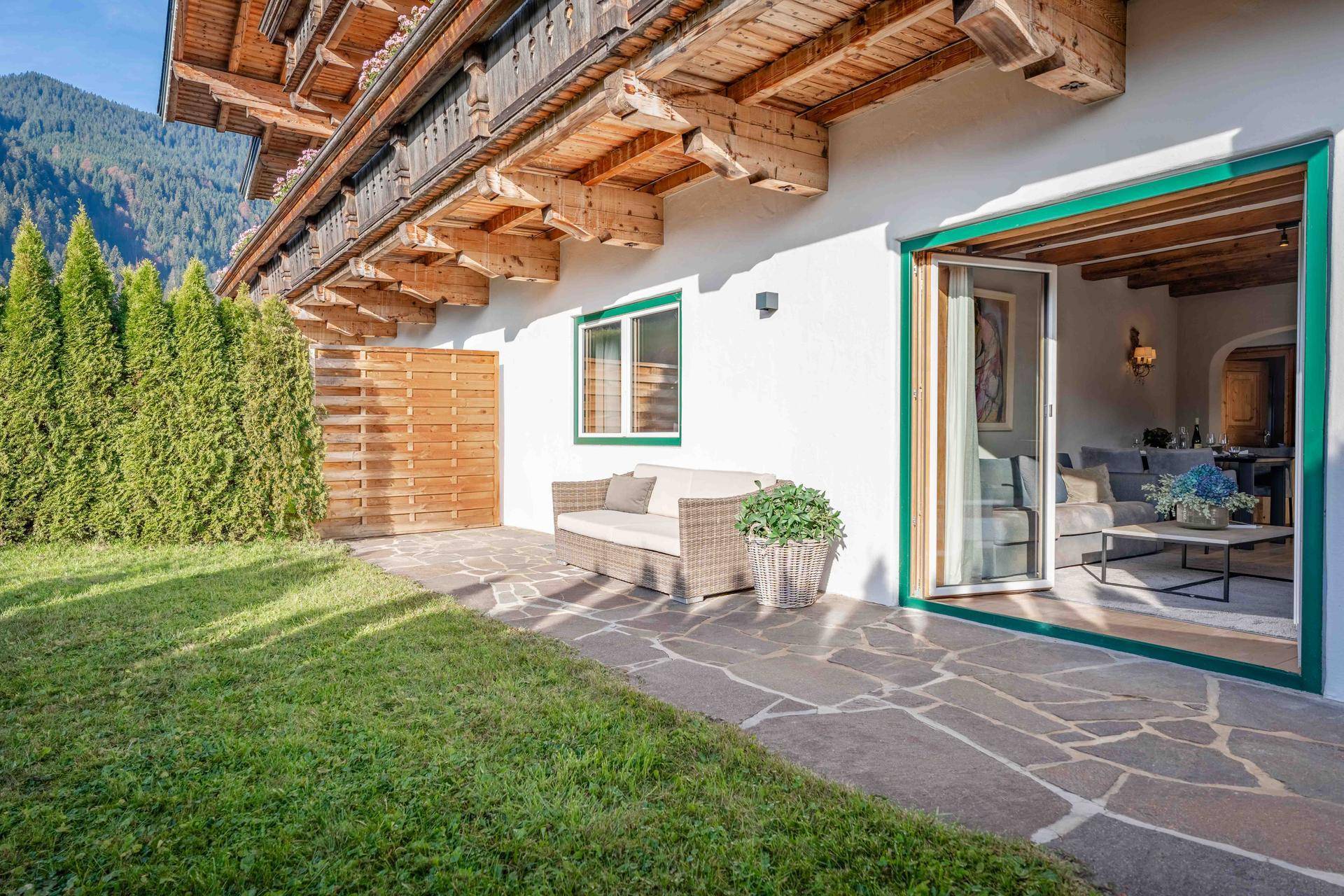 Gepflasterte Terrasse mit Gartenmöbeln, Rasenfläche und Blick auf die umliegende Natur.