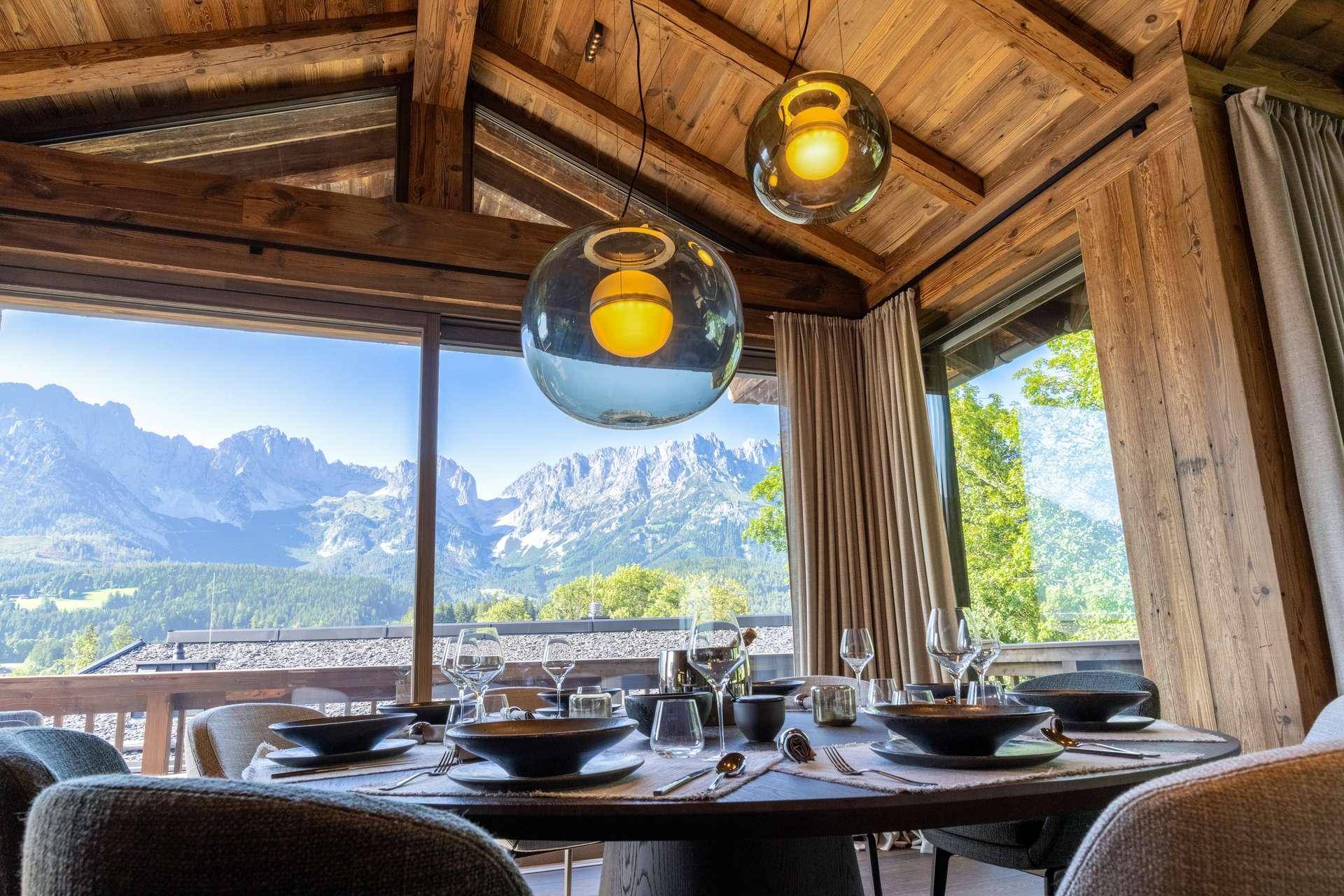 Eleganter Essbereich mit großem Tisch, modernen Pendelleuchten und atemberaubendem Bergblick.