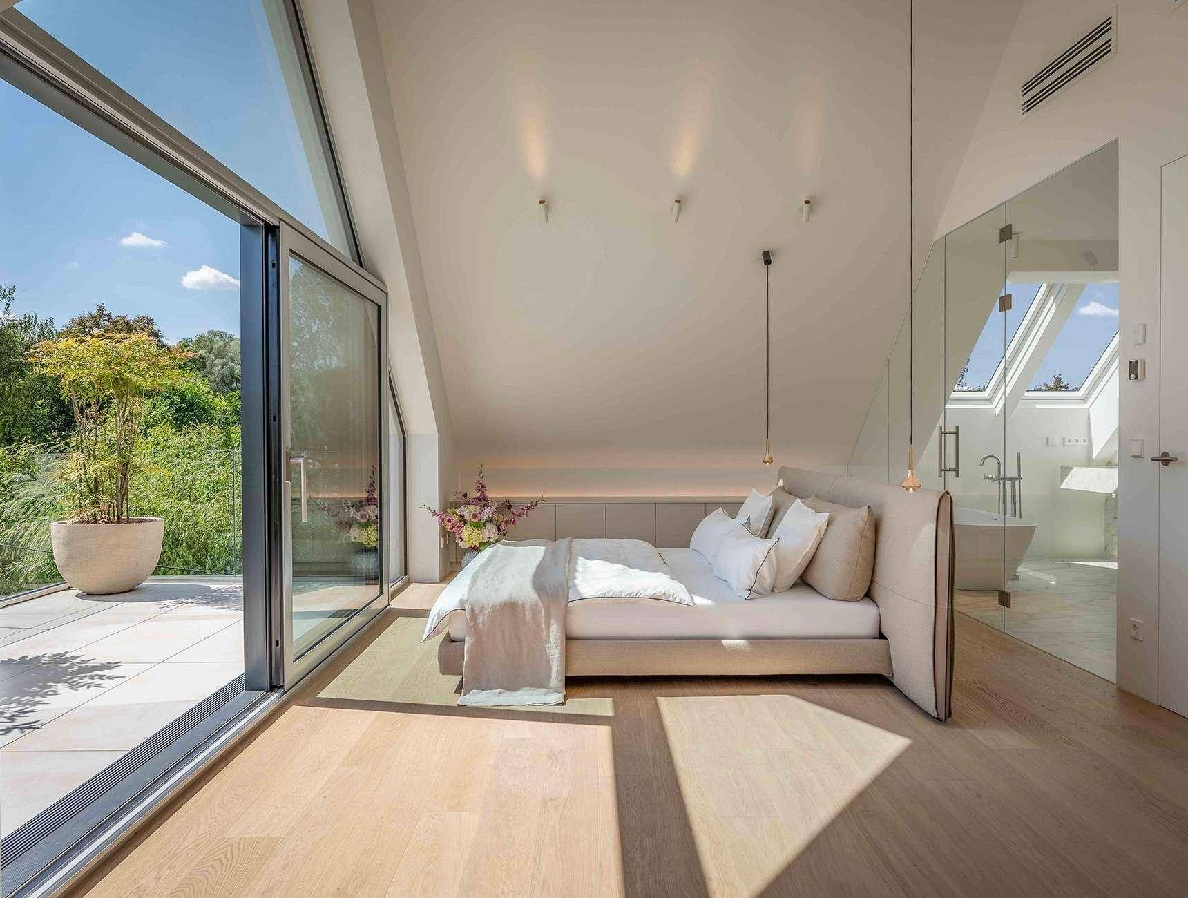 Helles Schlafzimmer mit Dachschrägen, direktem Zugang zur Terrasse und offenem Badbereich.