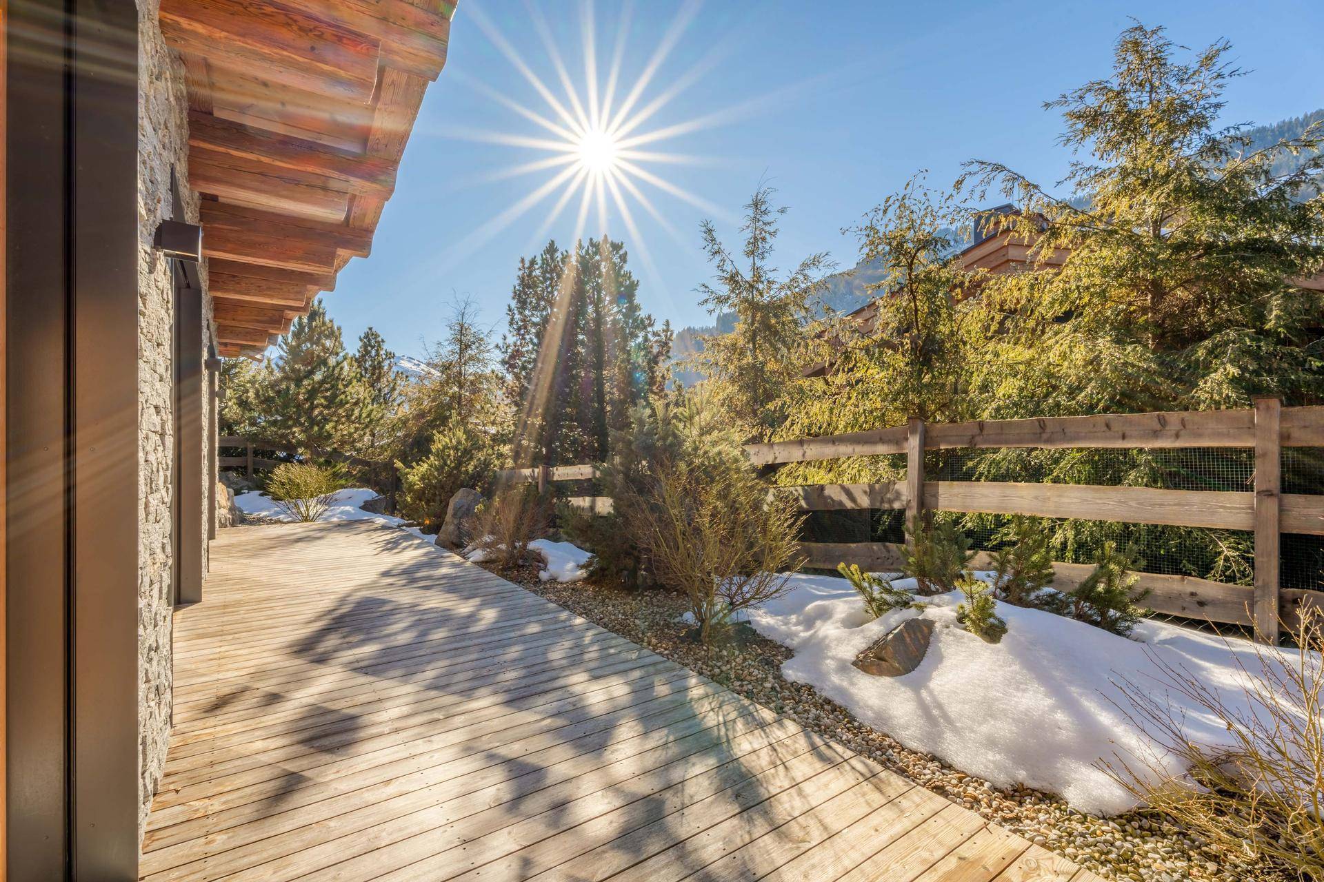 Sonnige Holzterrasse umgeben von winterlicher Natur und Bäumen, ideal für entspannte Stunden im Freien.
