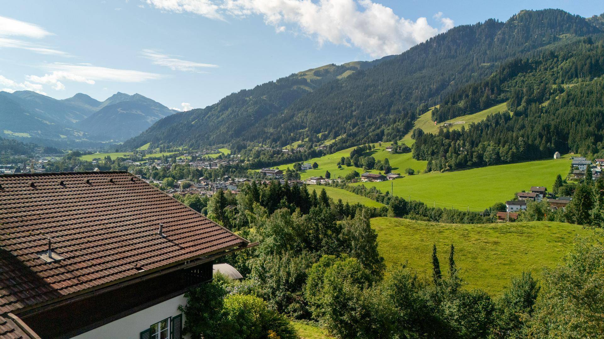 Panoramablick auf die umliegende Bergwelt und das idyllische Tal mit Wohnbebauung.