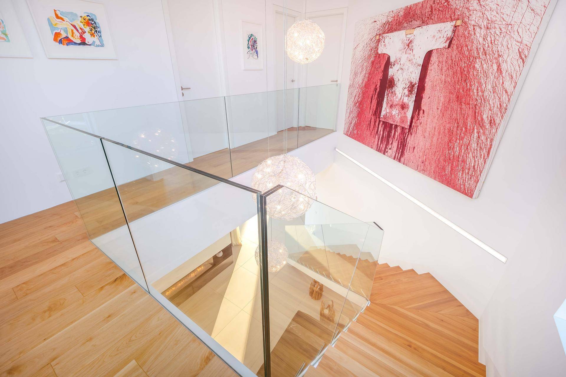Moderne Treppe mit Glasgeländer und Holzstufen, ergänzt durch zeitgenössische Kunstwerke an der Wand.