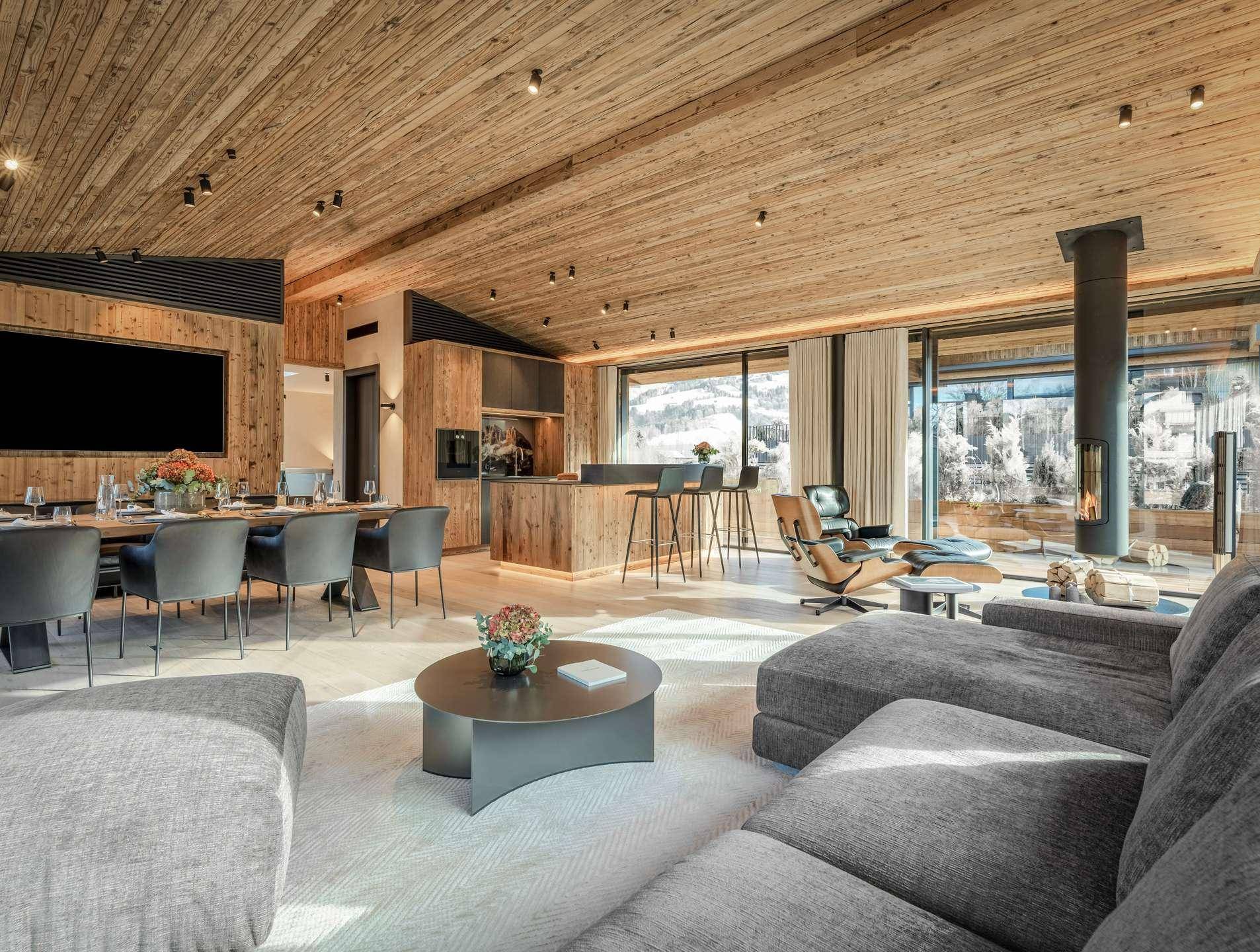Geräumiger offener Wohn-Essbereich mit Holzakzenten, modernem Kamin und Panoramablick auf die Berge.